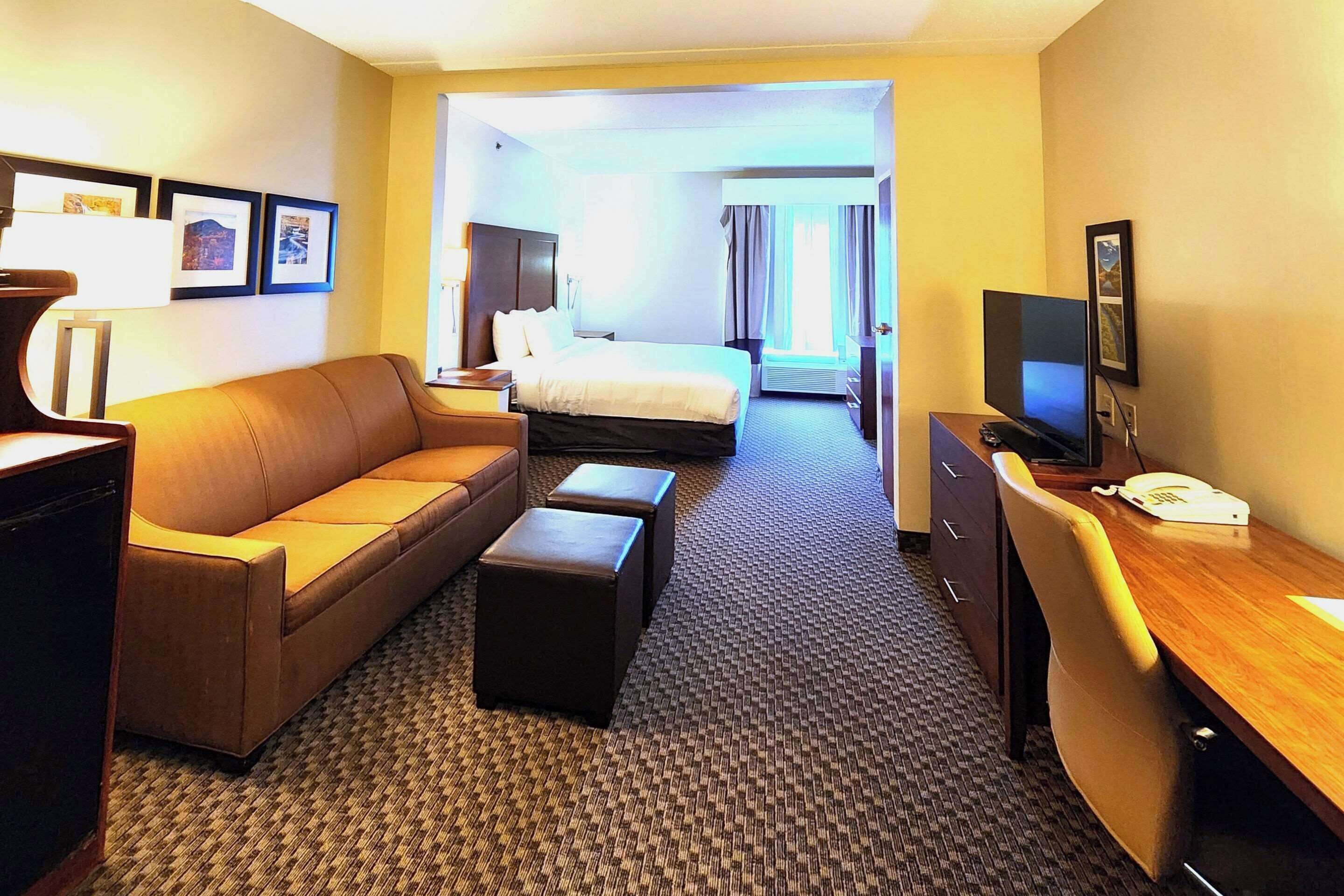 Quarto de hotel com cama, sofá, escrivaninha e televisão.