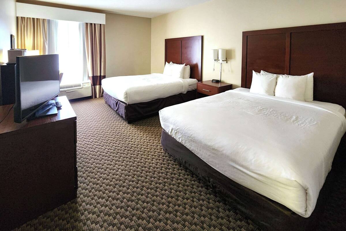 Habitación de hotel con dos camas, televisión, escritorio y ventana con cortinas.