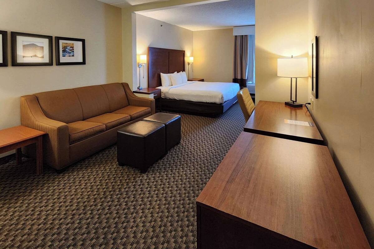 Habitación de hotel con un sofá de cuero marrón, un escritorio de madera, una cama con ropa blanca y una mesita.