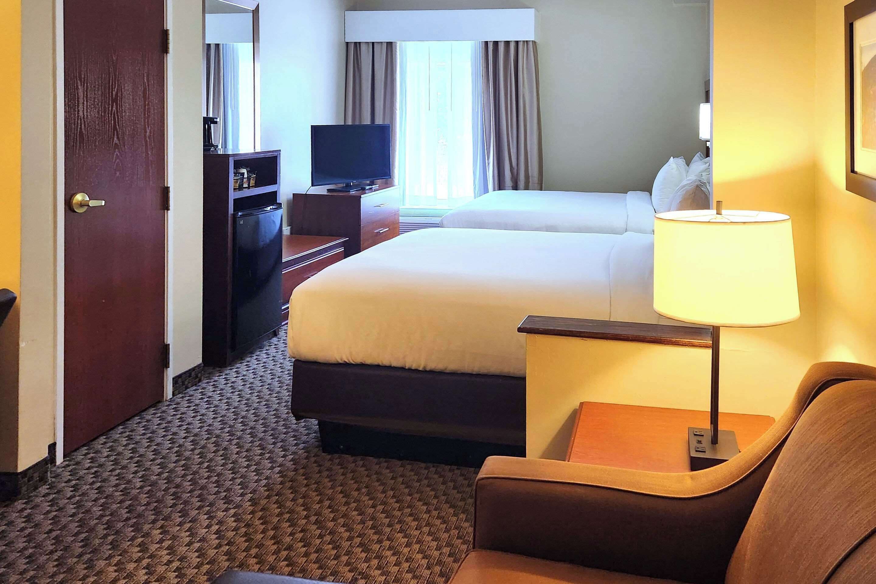 A hotel room with a bed, a TV on a dresser, a lamp, and a chair.