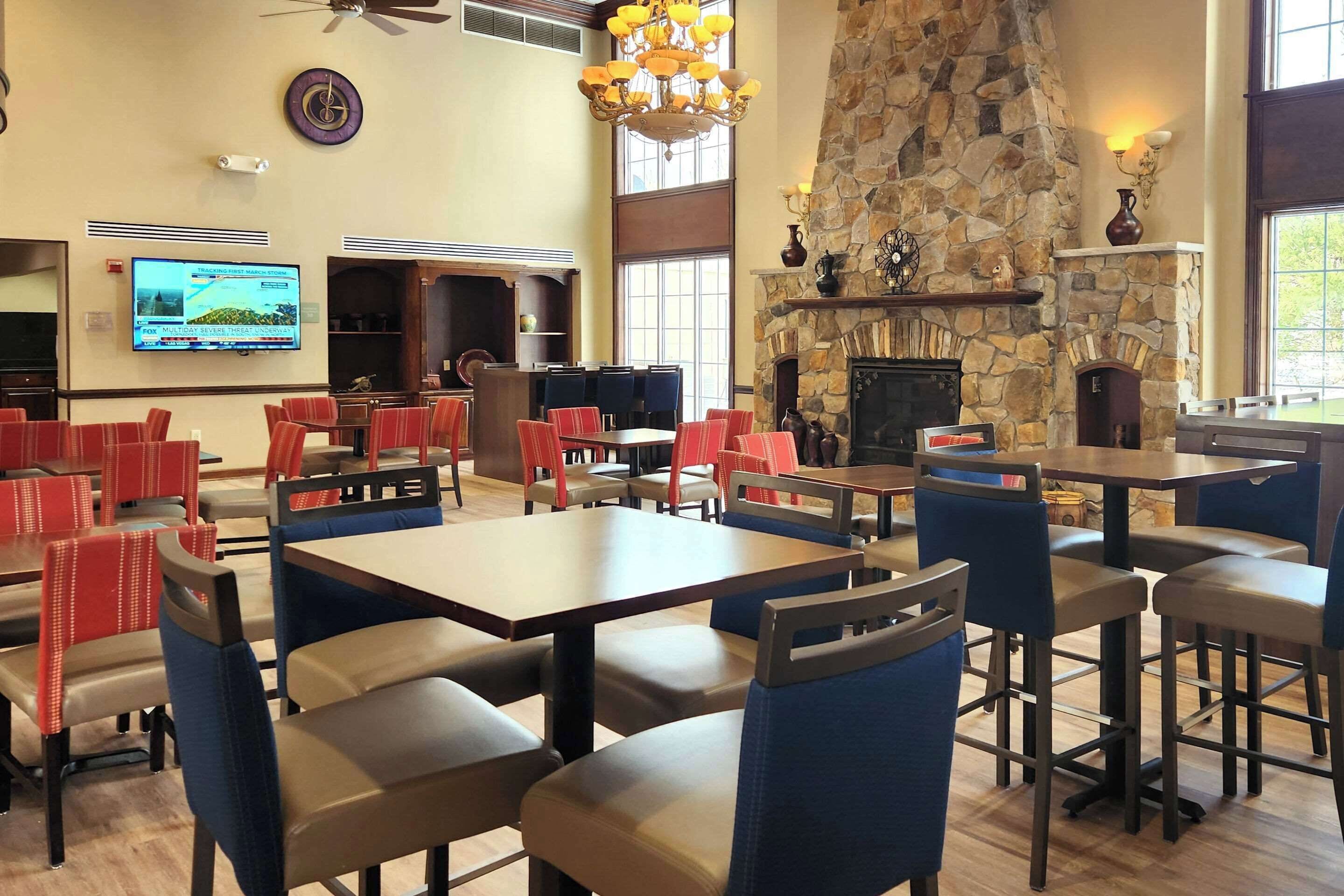 A restaurant with high ceilings, stone walls, and a fireplace. Tables and chairs are arranged for dining.