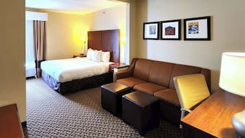 A hotel room with a bed, a sofa, a desk, and a lamp. There are framed pictures on the wall.