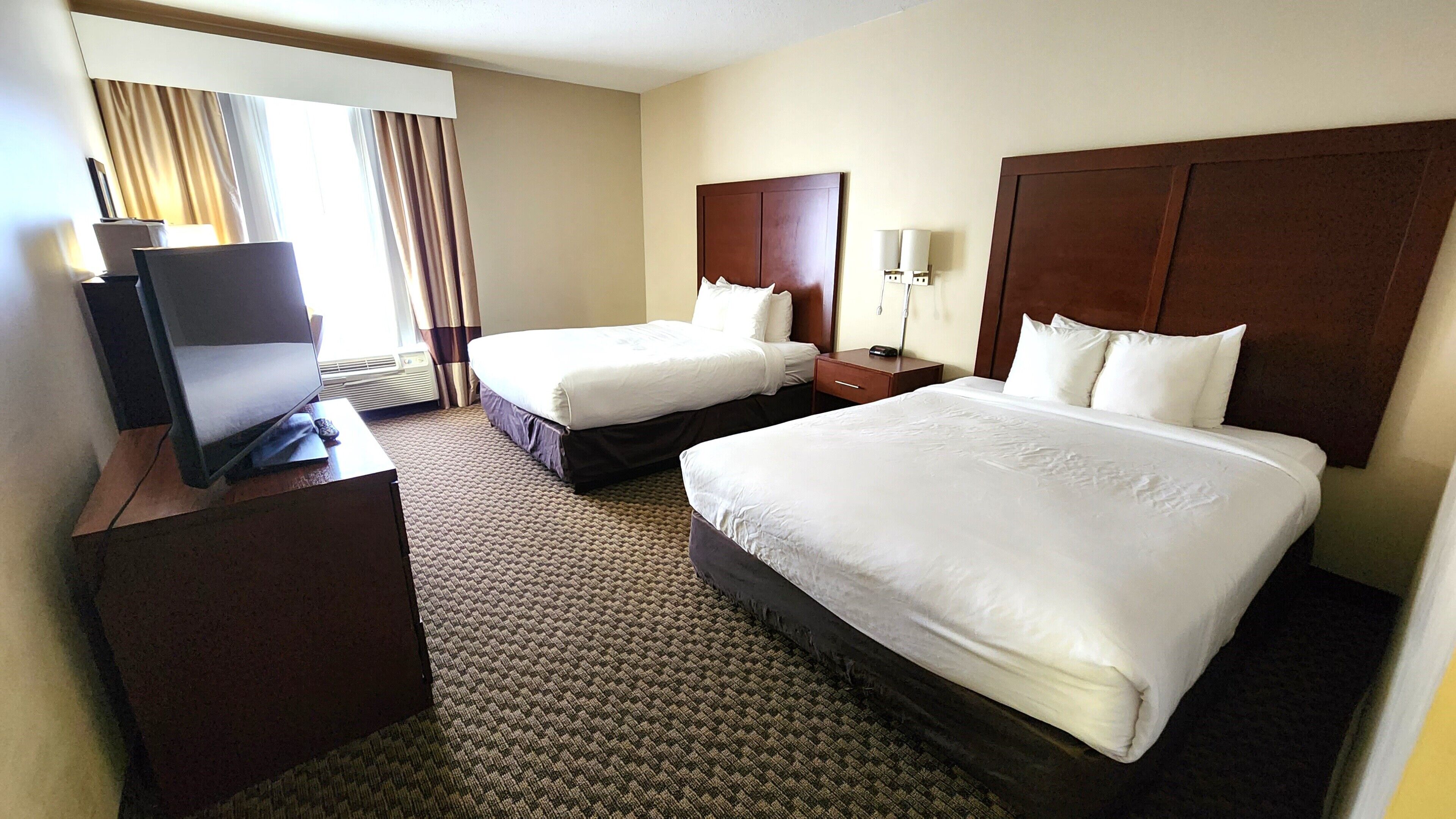 A hotel room with two beds, a TV, a desk, and a window with curtains.