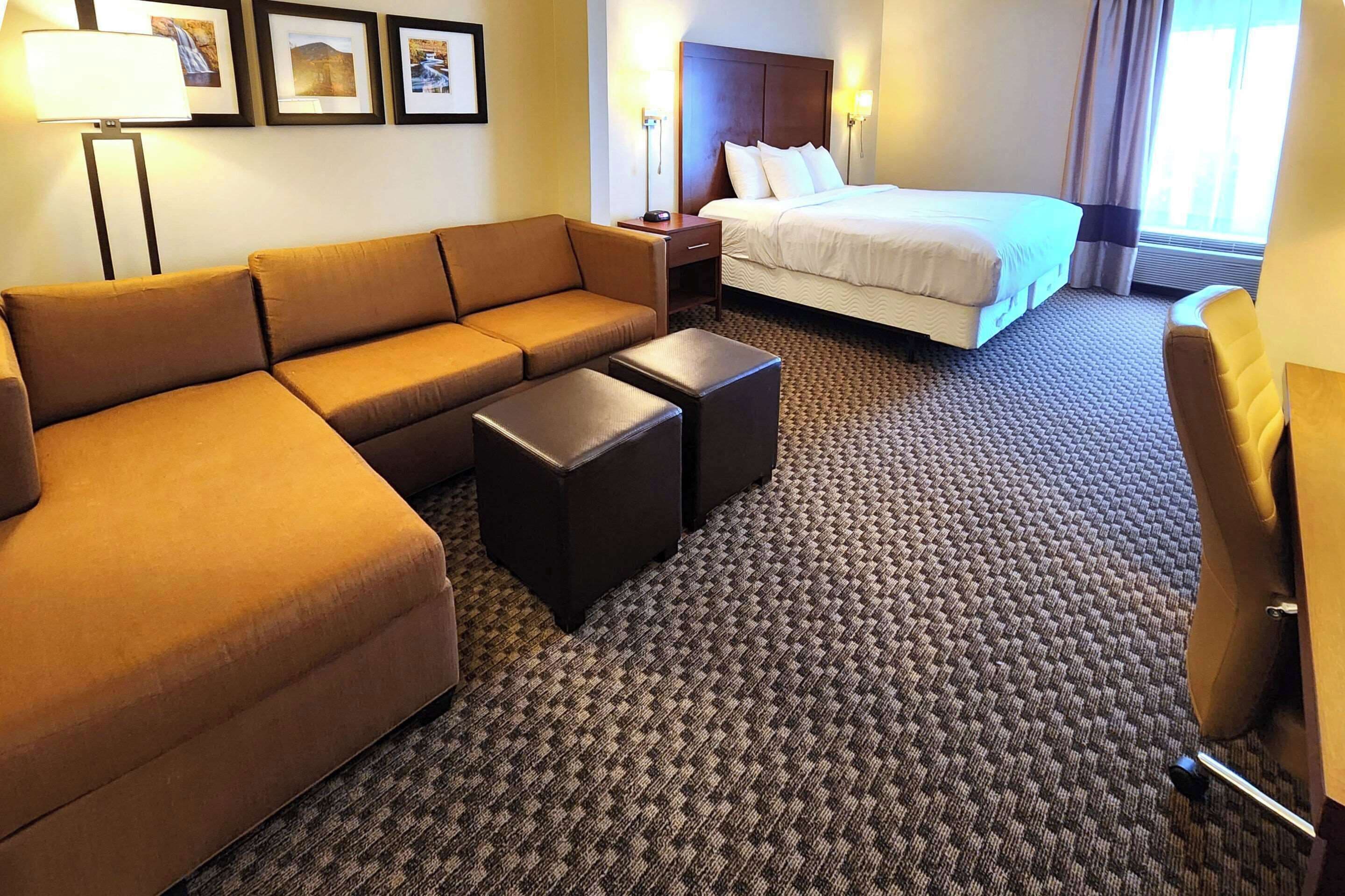 A hotel room with a sofa, two ottomans, a bed, a nightstand, and framed pictures on the wall.