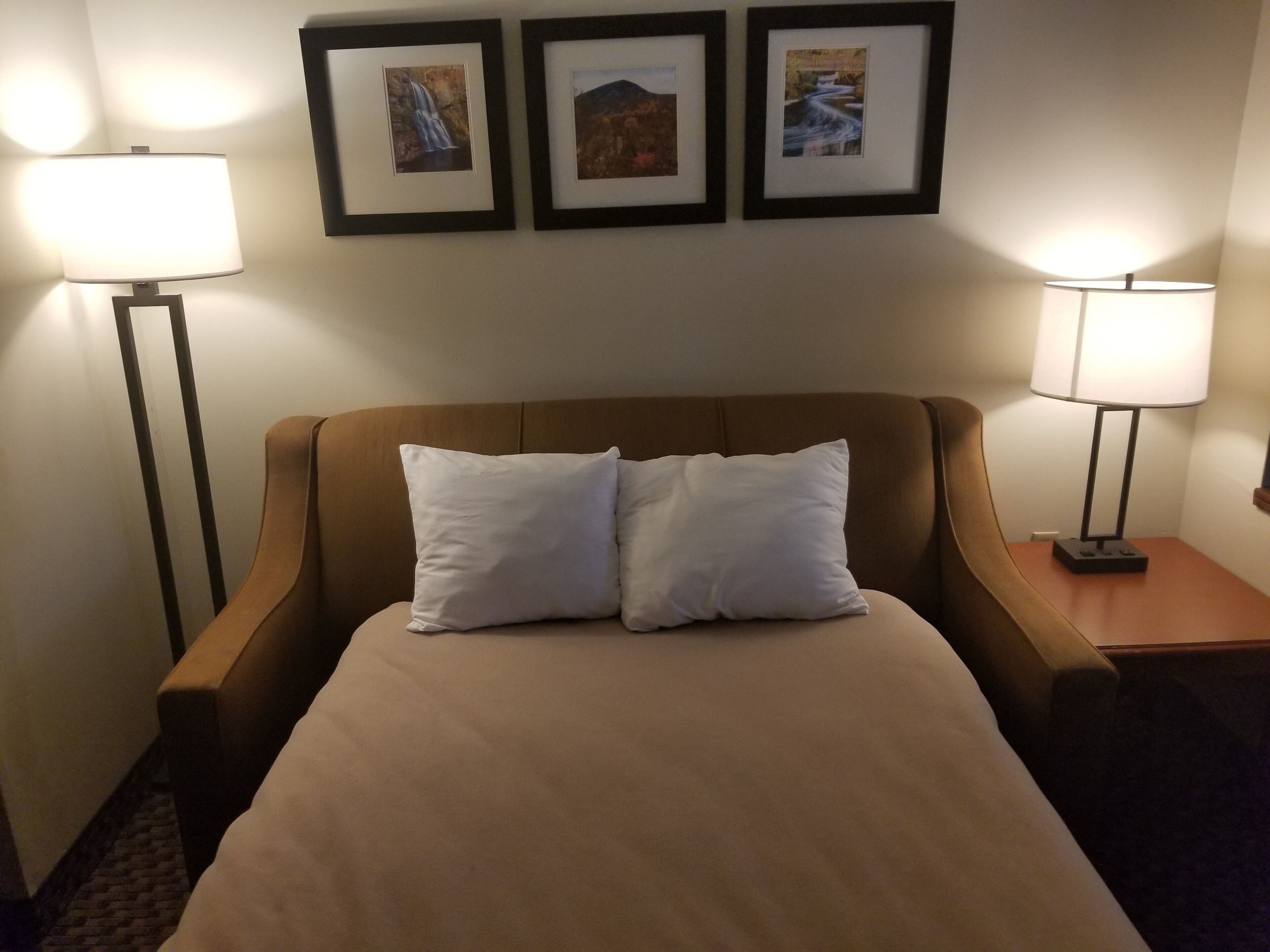 Una habitación de hotel con una cama grande, dos lámparas de noche y tres cuadros en la pared.