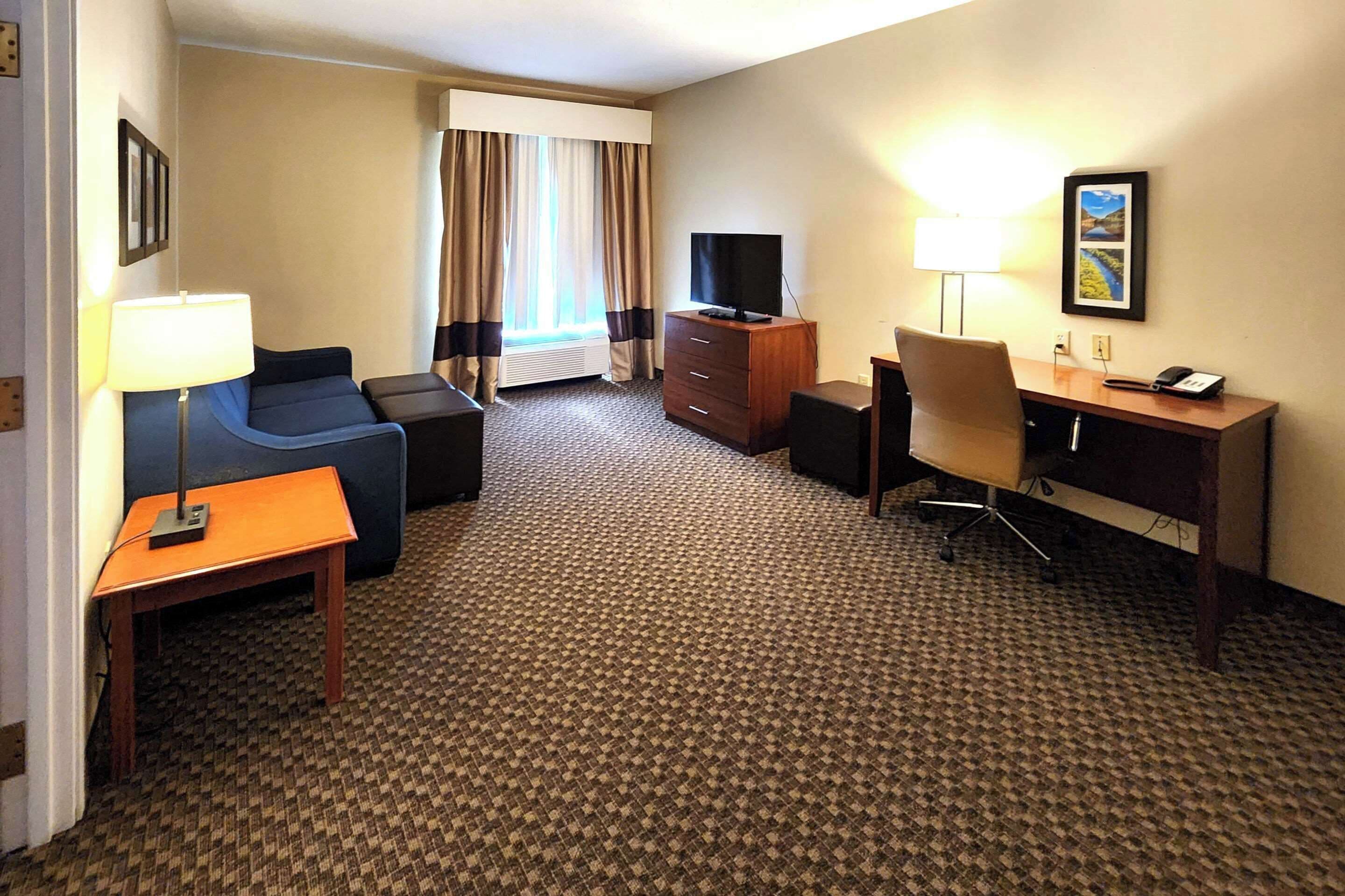 A hotel room with a sofa, a desk, a television, a lamp, and a carpeted floor.