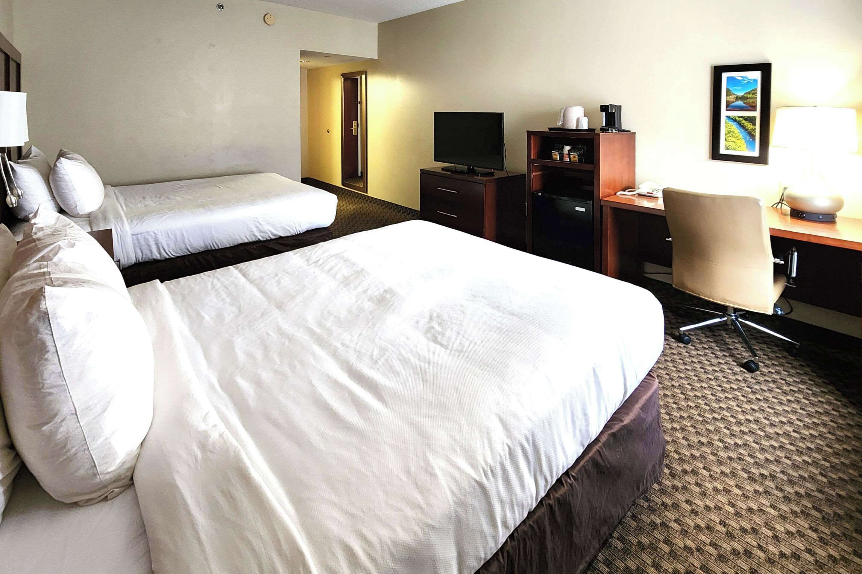 A hotel room with two beds, a desk with a chair, a television, and a framed picture on the wall.