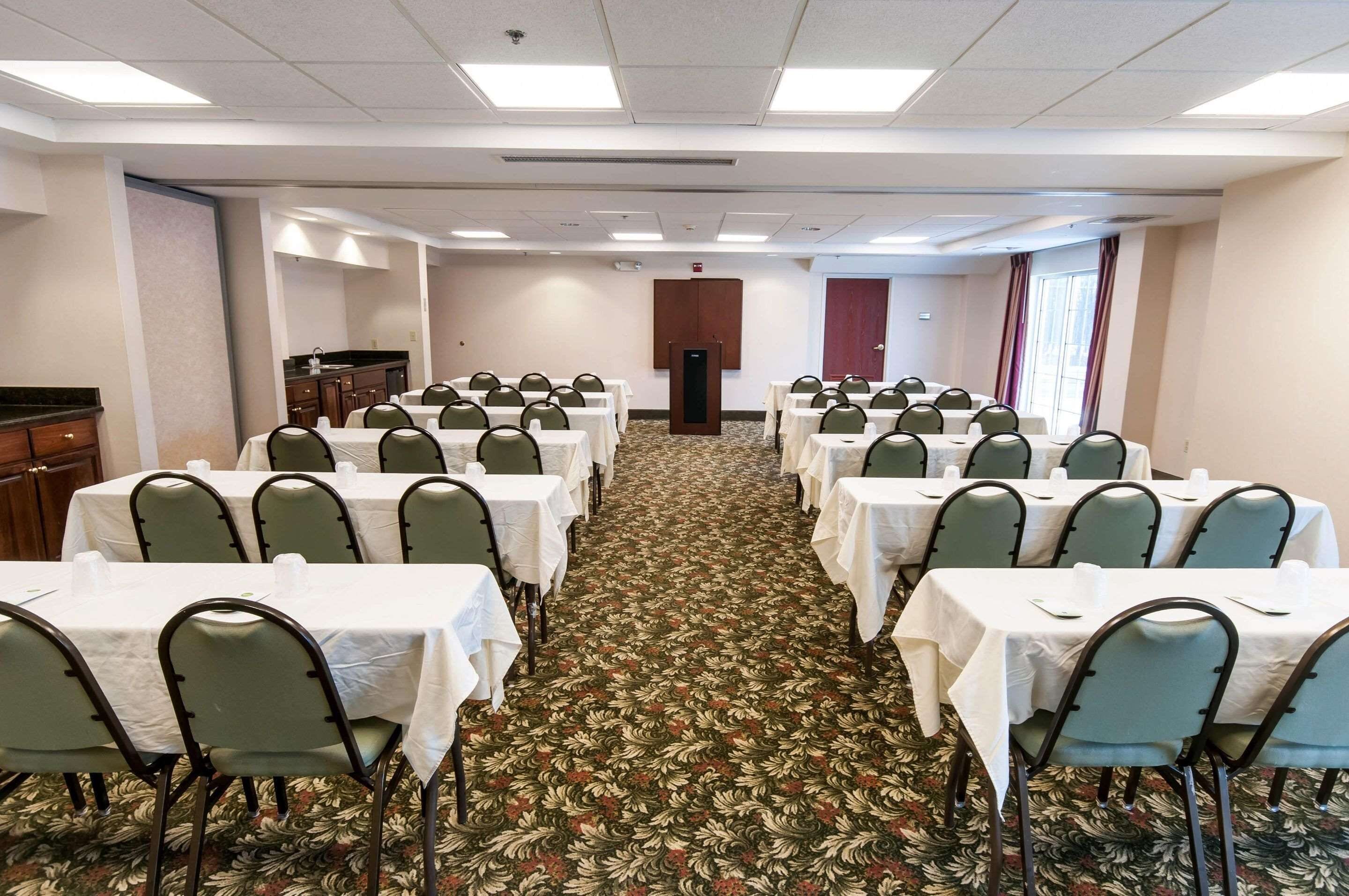 A conference room with rows of tables and chairs, a carpeted floor, and a door in the background.