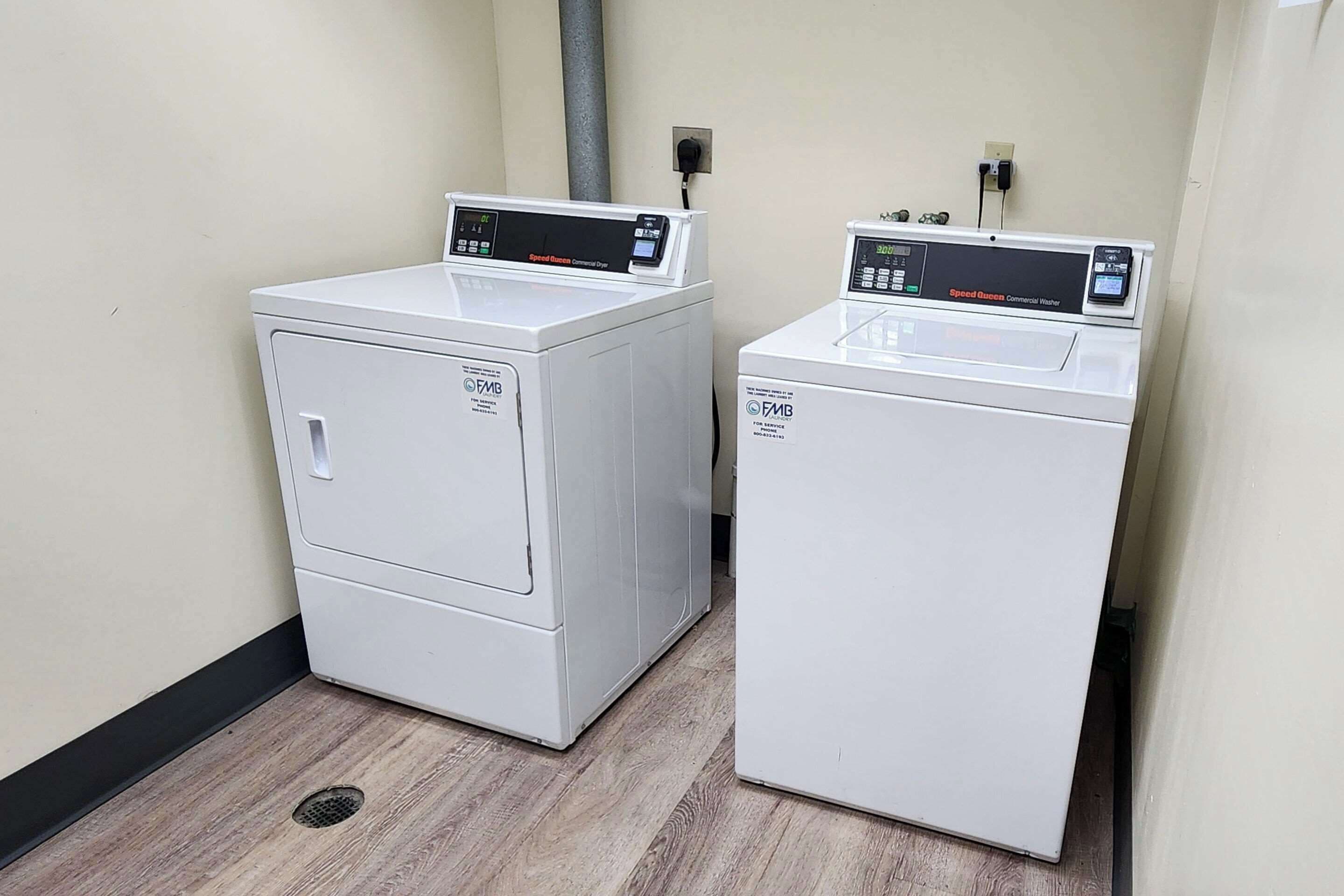 Two front-loading washing machines in a laundry room with a wooden floor and beige walls.
