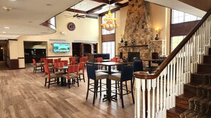 A spacious dining area with high ceilings, a stone fireplace, and a staircase with white balusters.