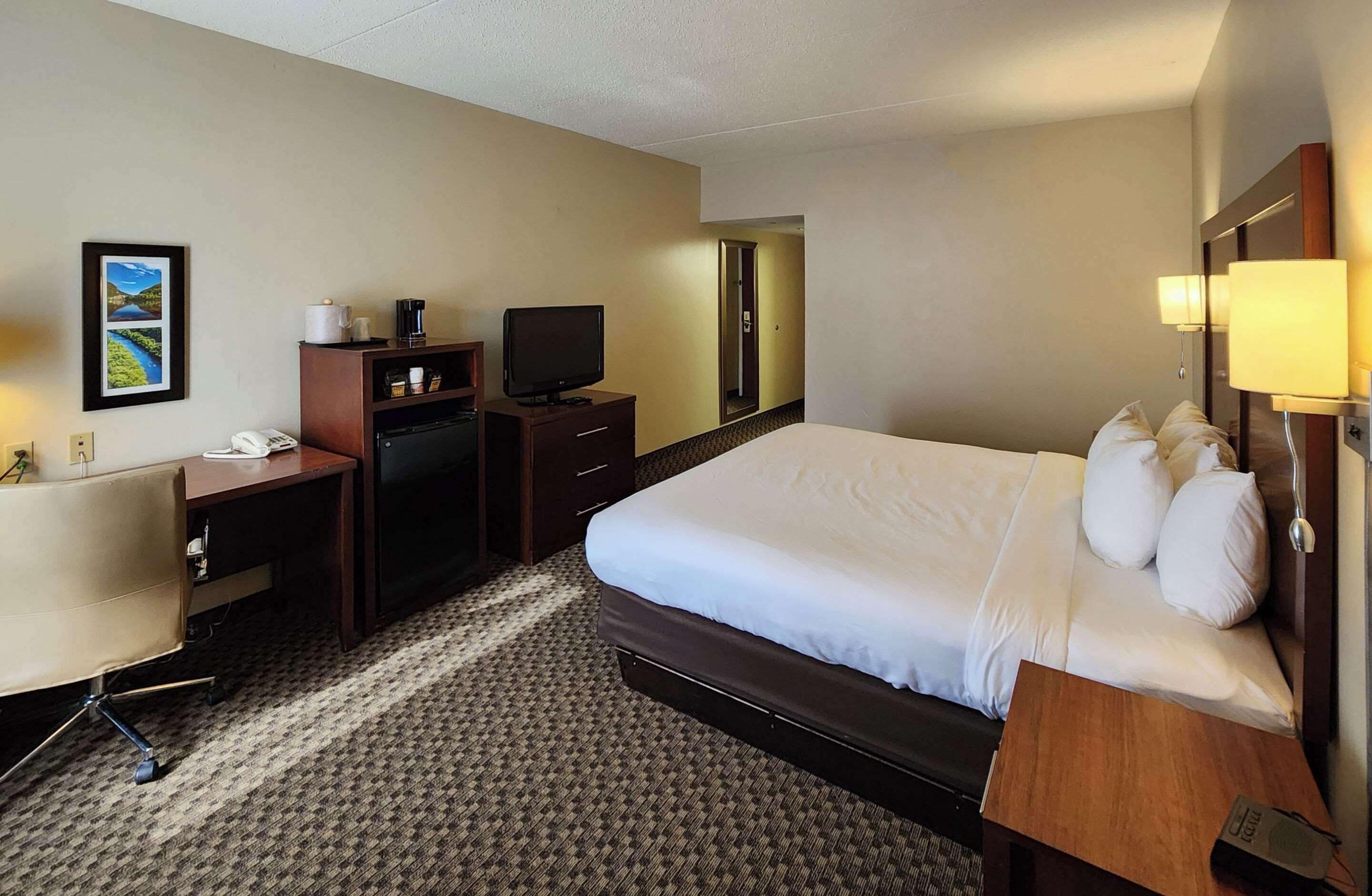 A hotel room with a large bed, a desk with a telephone, a television, and a mirror.