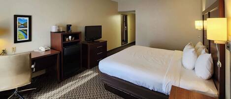 A hotel room with a large bed, a desk with a telephone, a television, and a mirror.