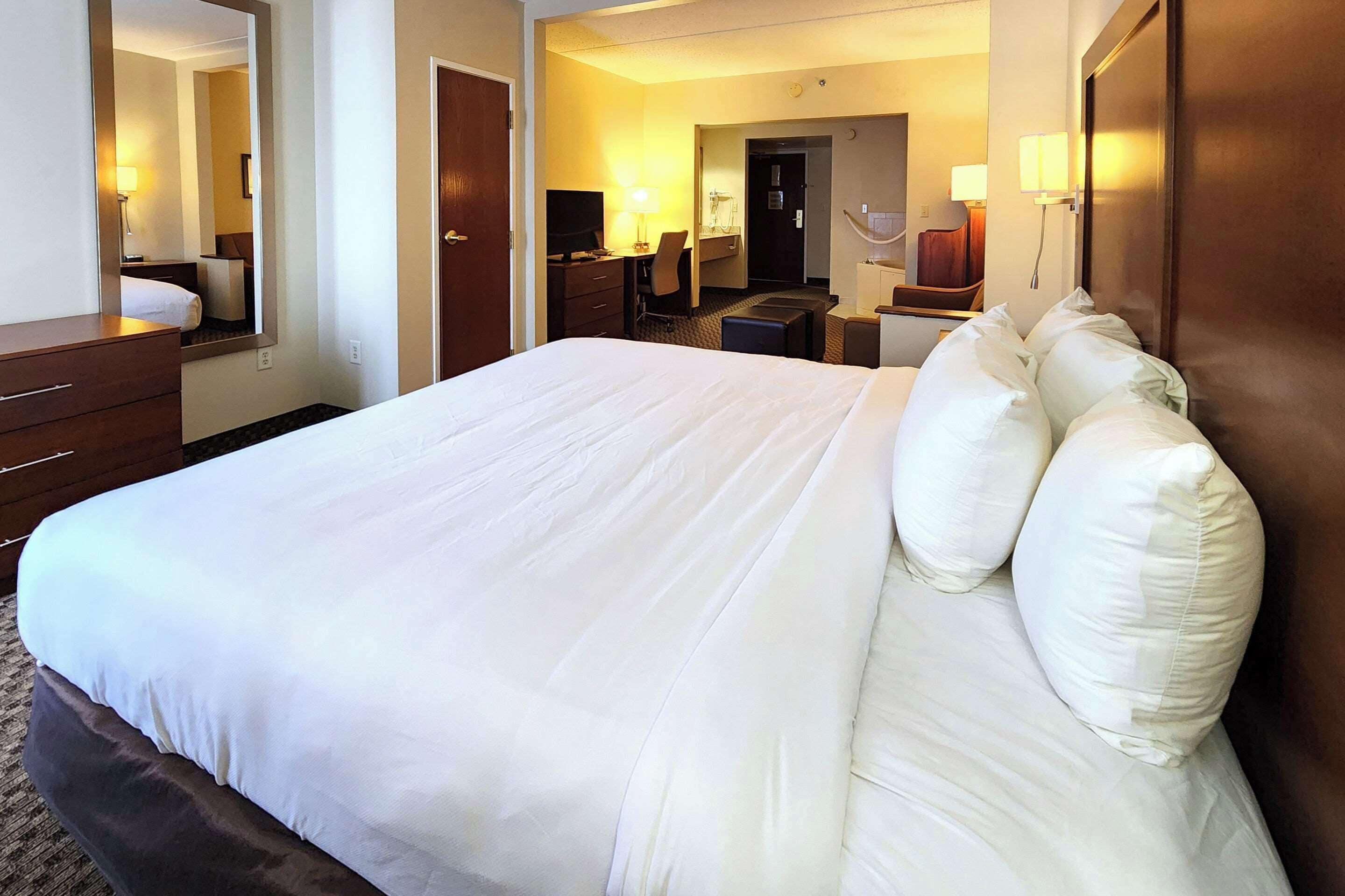A hotel room with a large bed, a desk with a chair, a television, and a mirror.