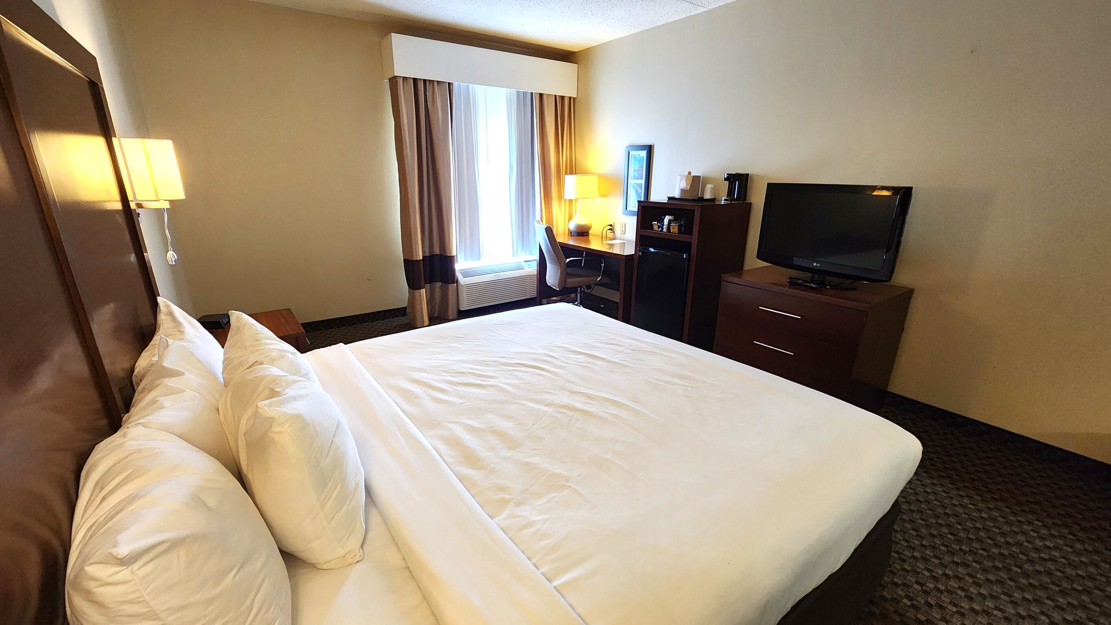 A hotel room with a large bed, a desk with a chair, a television, and a window with curtains.