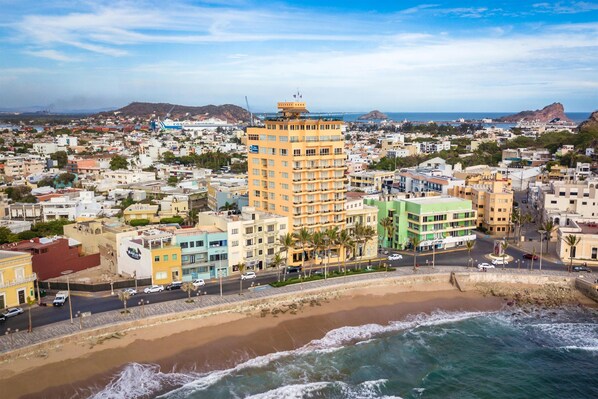 Paisagem costeira urbana com um edifício amarelo destacado, uma praia e vista para o oceano.
