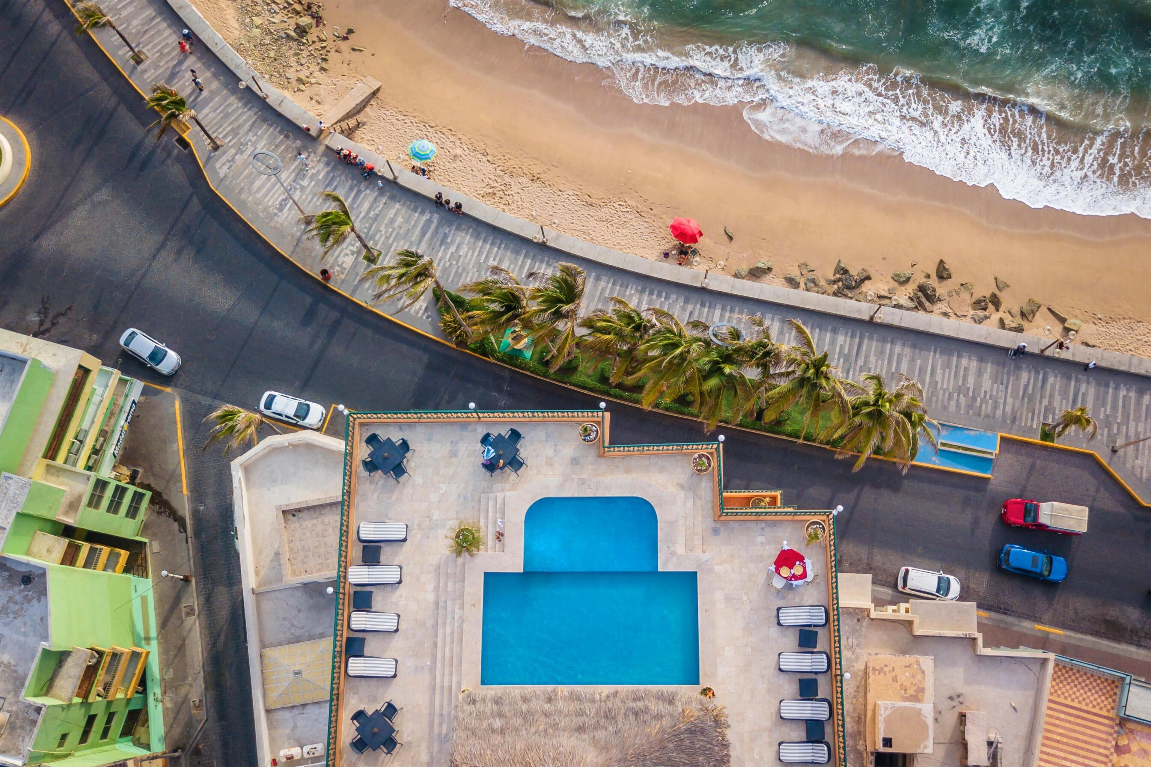 Vista aérea de un hotel costero con piscina, acceso a la playa y una carretera con vehículos.