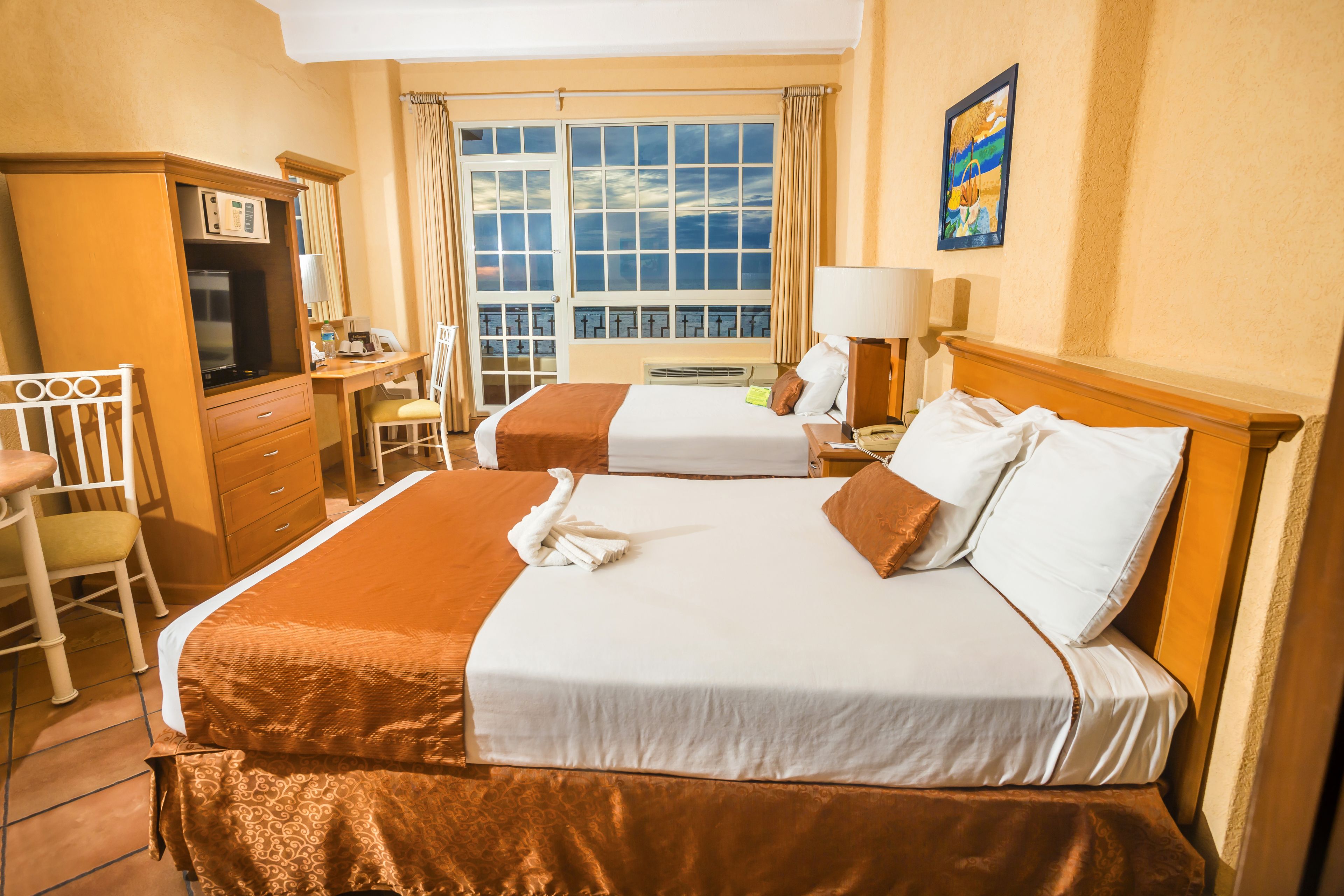 A hotel room with two beds, a desk, a chair, a television, and a window with curtains.