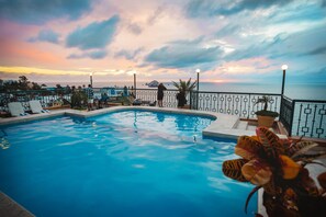 Piscina com vista para o mar e um pôr do sol.