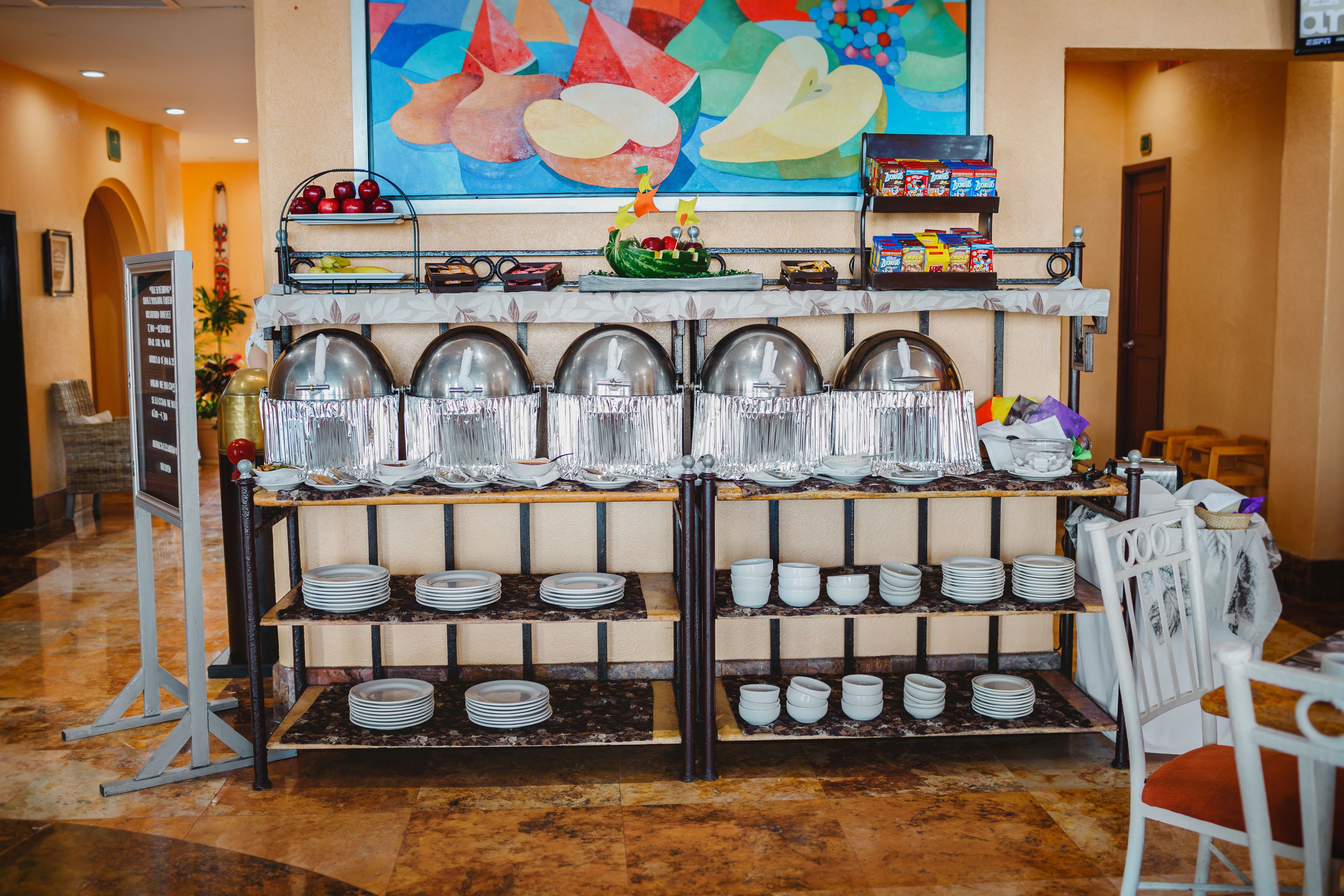 A buffet setup with multiple serving stations, a menu board, and a colorful abstract painting on the wall.