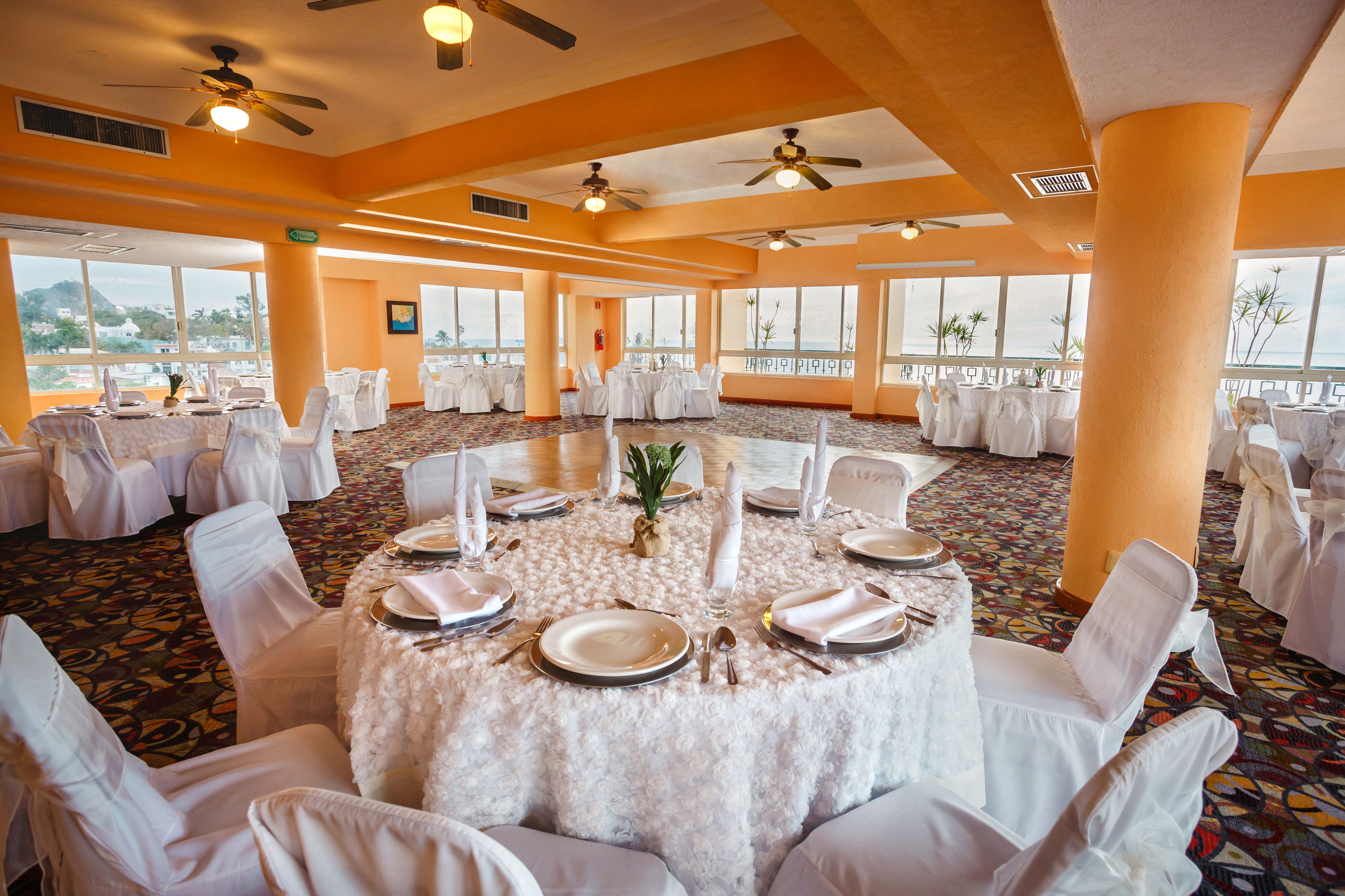 A banquet hall with round tables set for a formal event, featuring white tablecloths, chairs, and centerpieces.
