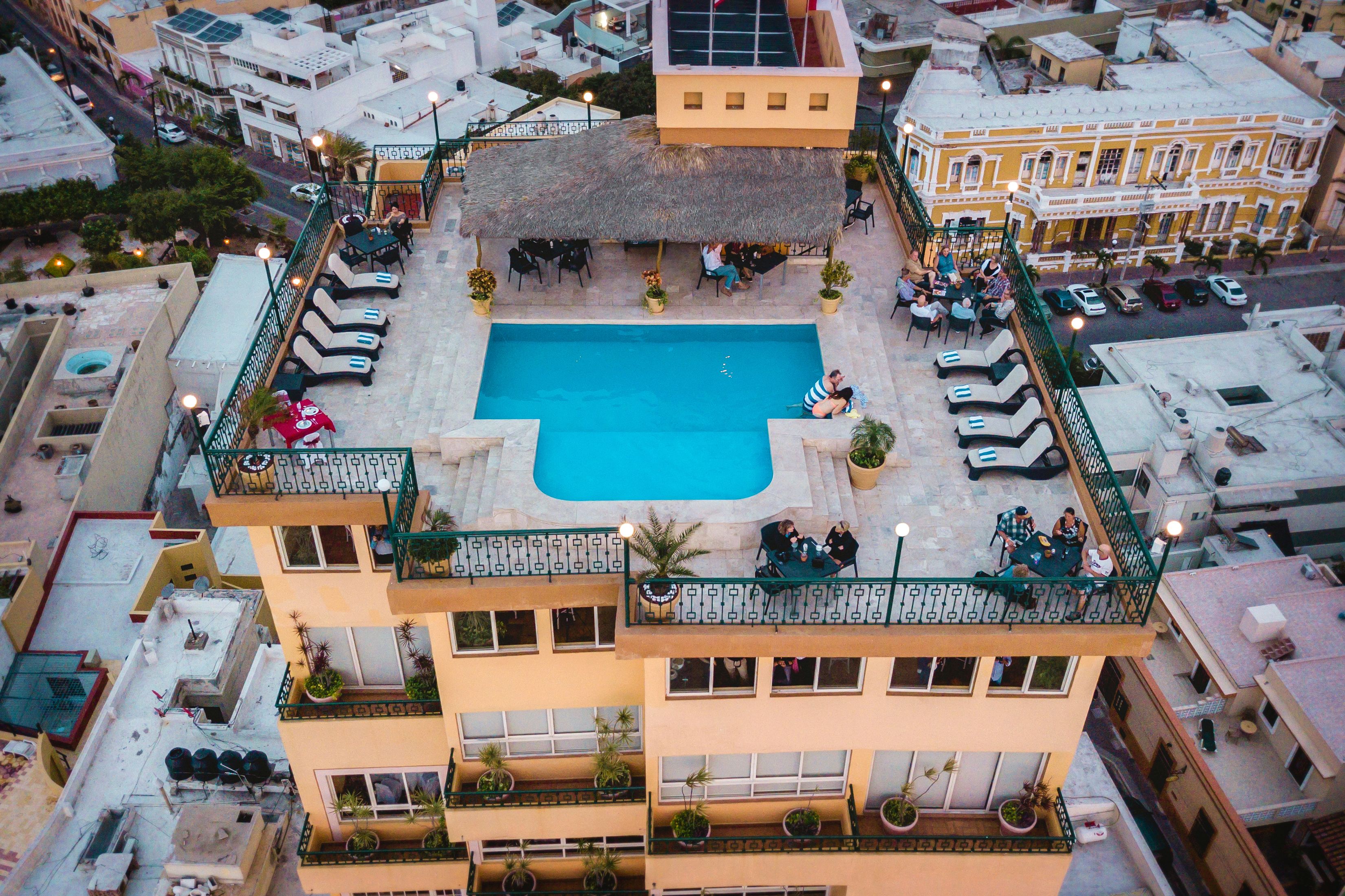 Ein Hochhaus-Hotel mit einem Pool auf dem Dach, Außenbereich zum Sitzen und mehreren Balkonen mit Pflanzen.