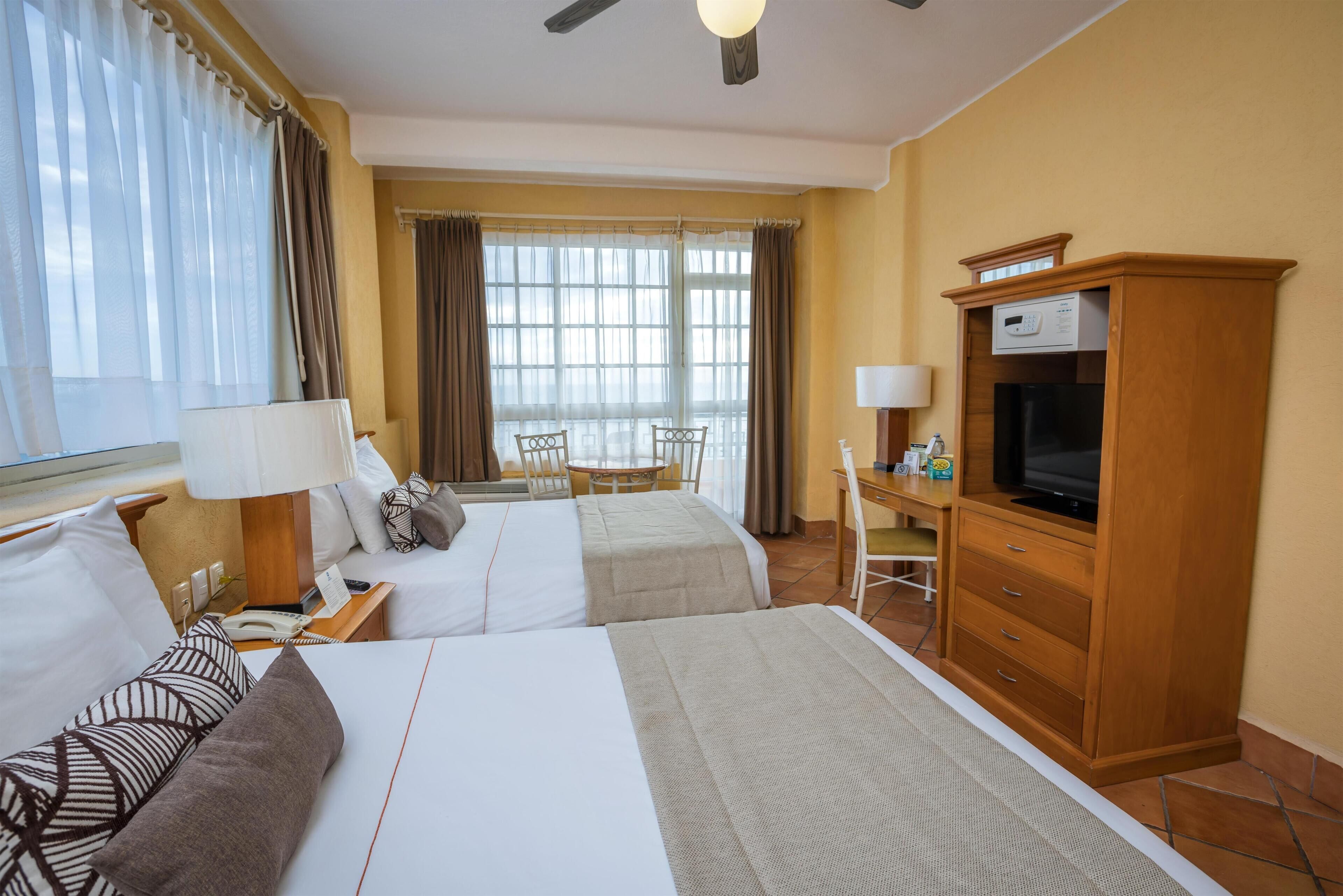 Habitación de hotel con dos camas, un escritorio, un televisor y vistas al exterior.