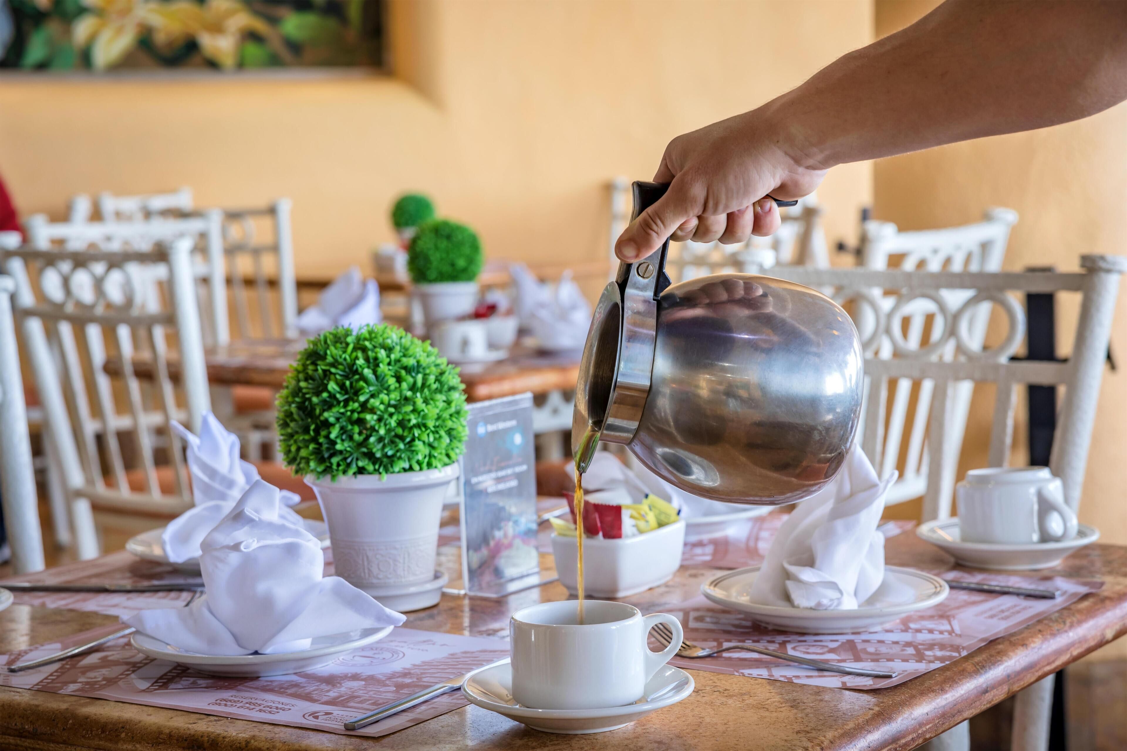 A table set for a meal with a white cup and saucer, a small white bowl, and a potted plant.