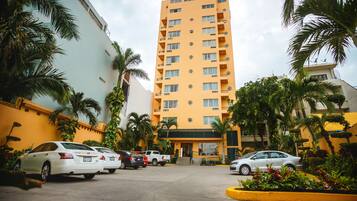 Un hotel de varios pisos con fachada amarilla, coches estacionados y palmeras.
