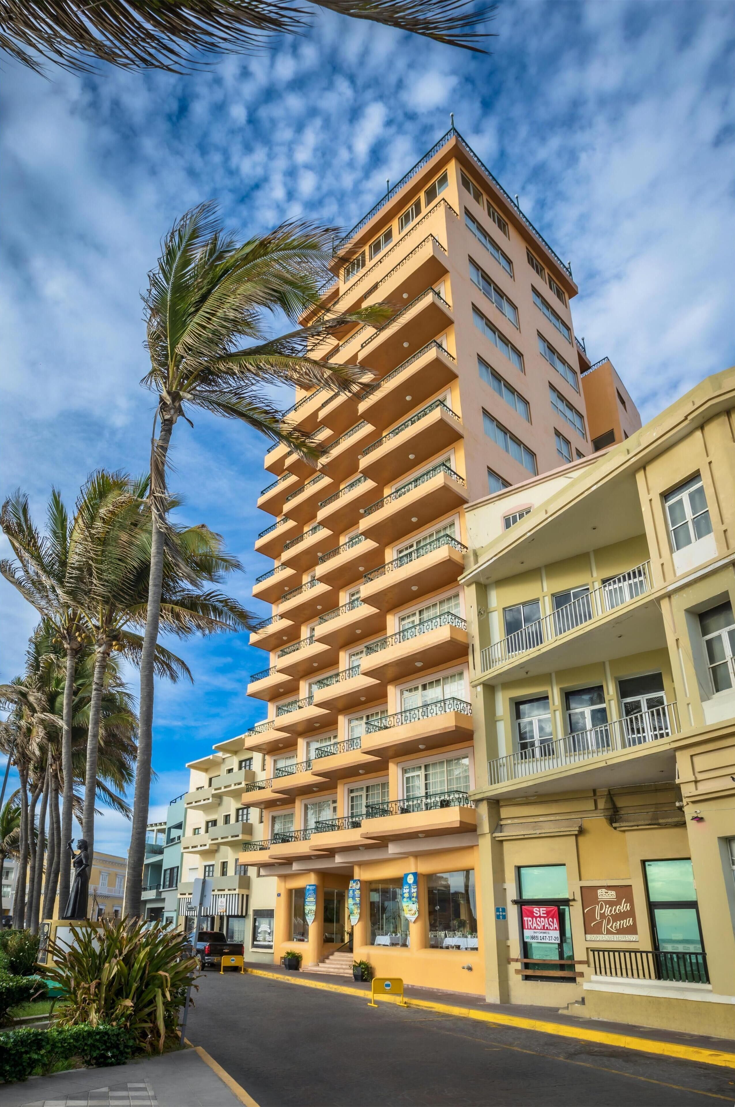 Ein mehrstöckiges Hotel mit Balkonen, Palmen und blauem Himmel.
