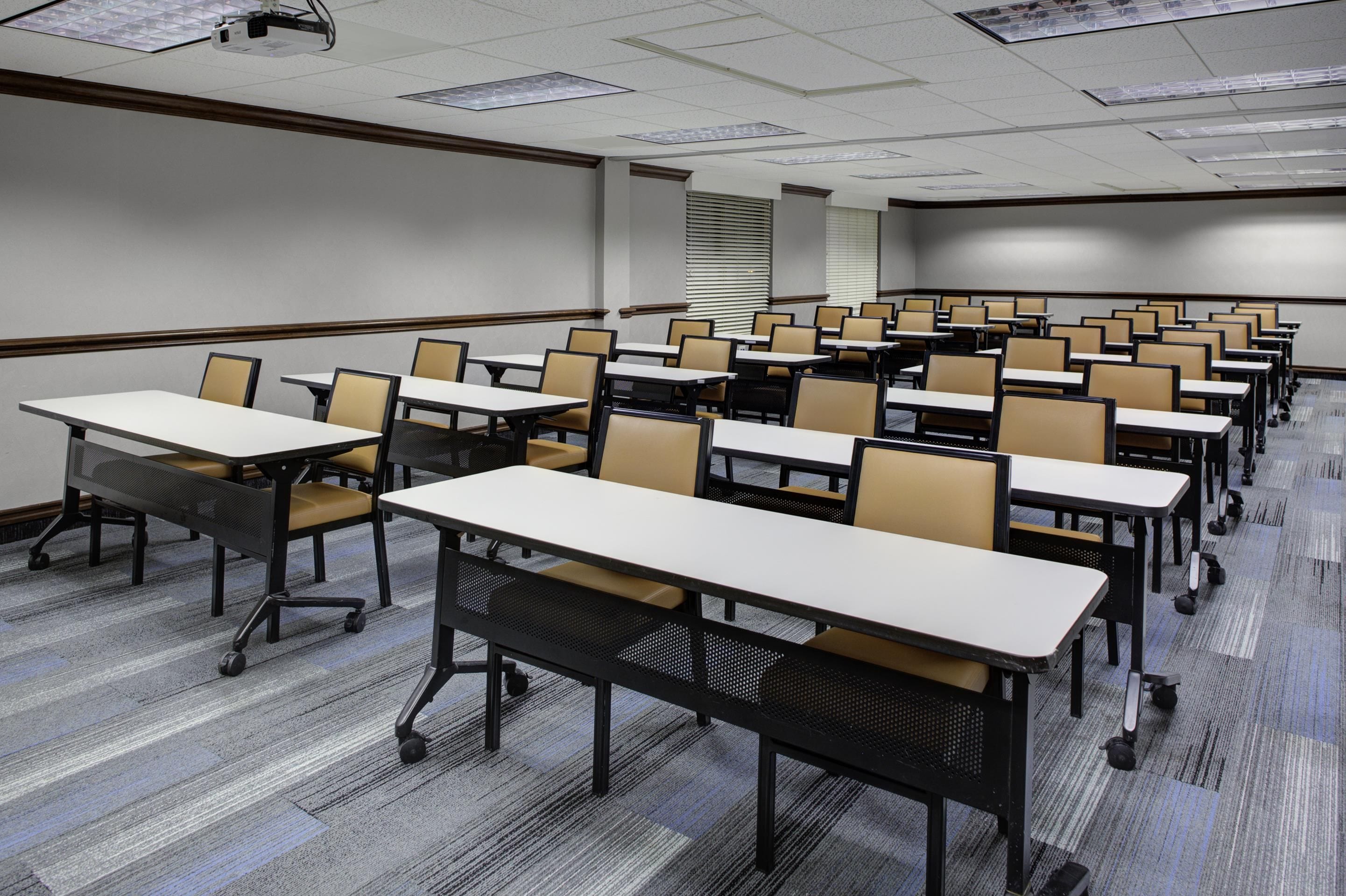 A conference room with rows of tables and chairs, carpeted flooring, and a projector screen.