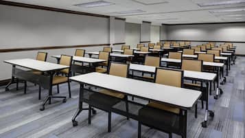 A conference room with rows of tables and chairs, carpeted flooring, and a projector screen.