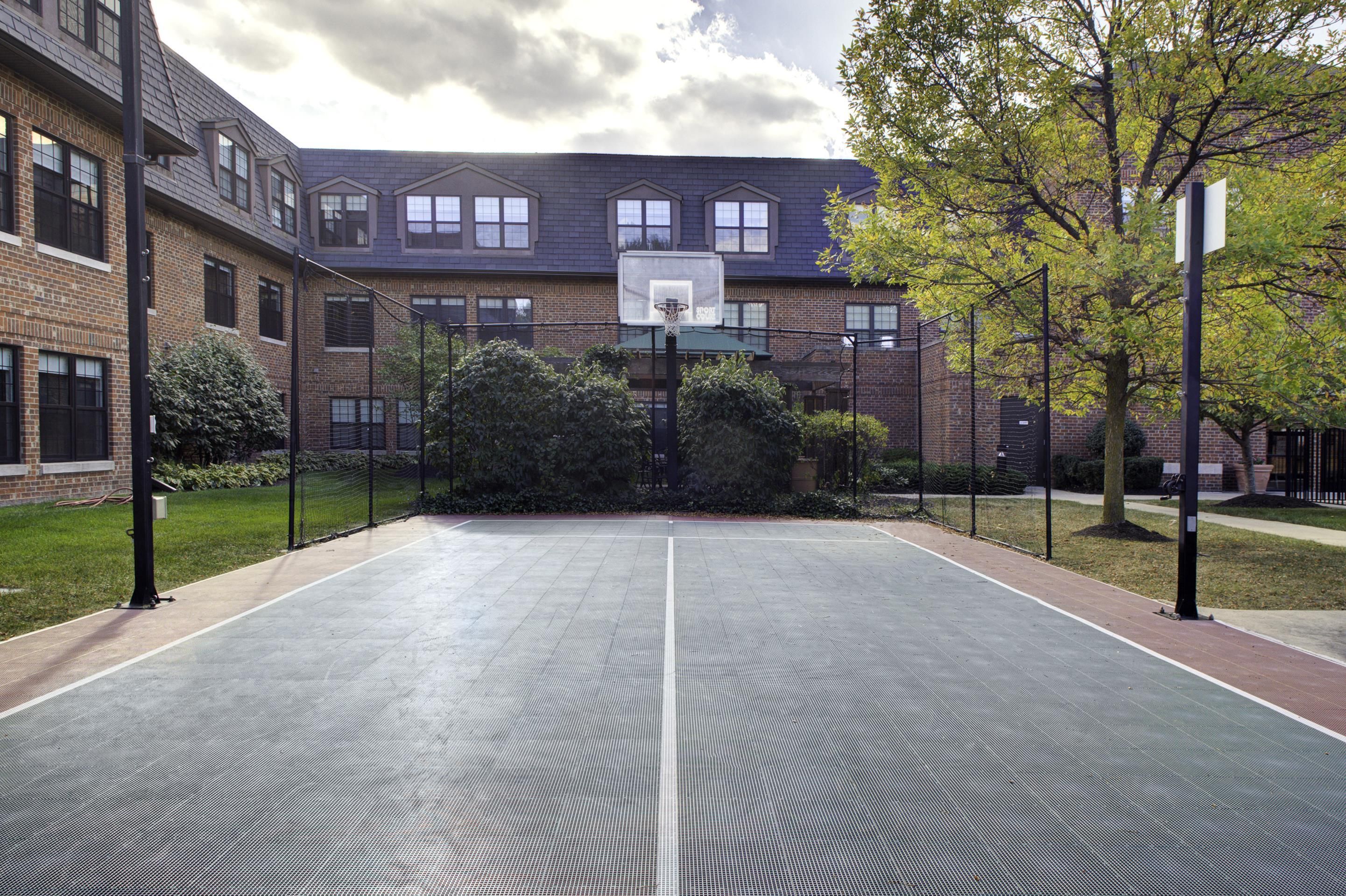Un campo da basket all'aperto con canestro e rete, circondato da un edificio in mattoni con diverse finestre.