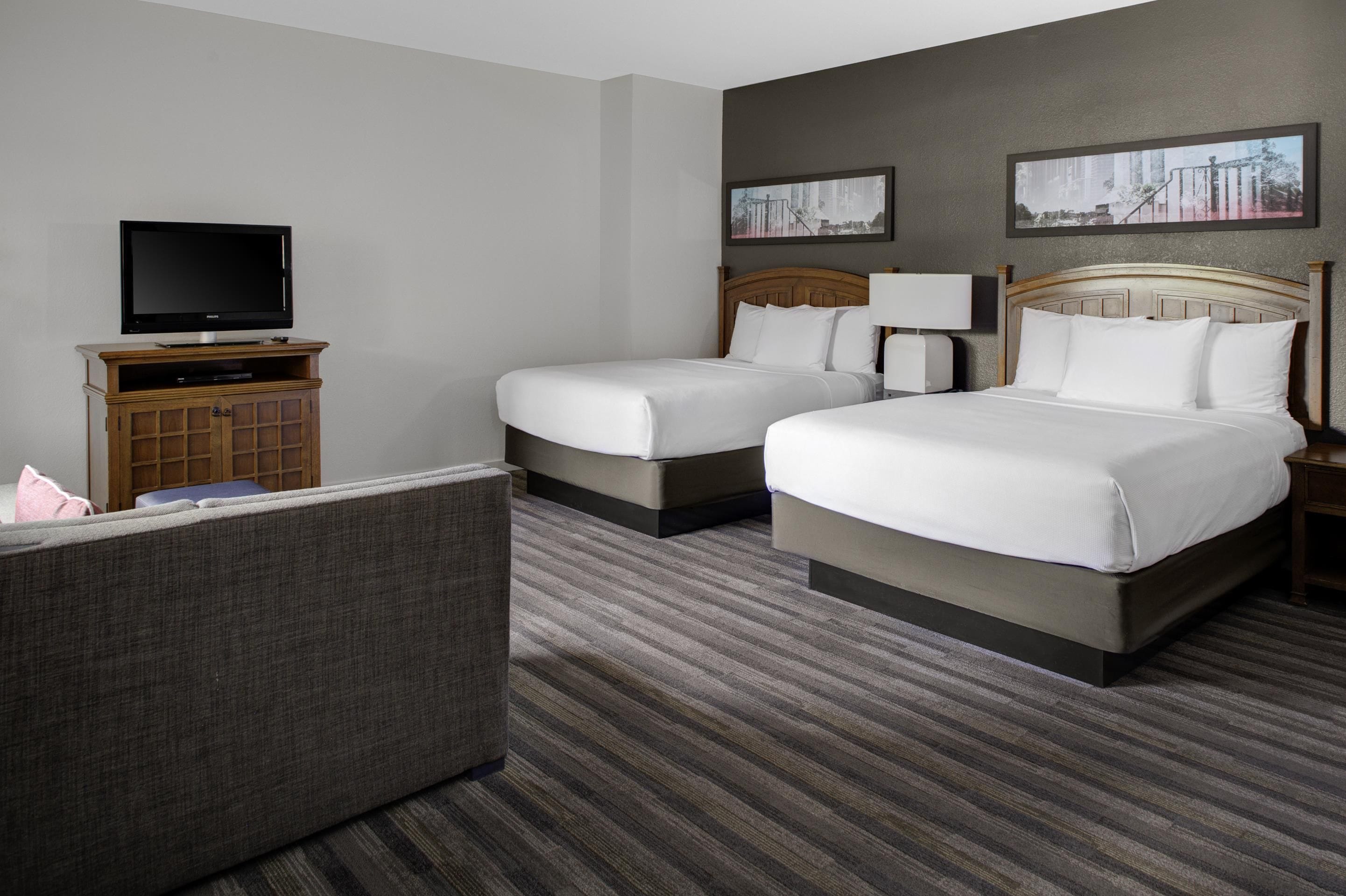 Una habitación de hotel con dos camas, televisión, escritorio y sofá.
