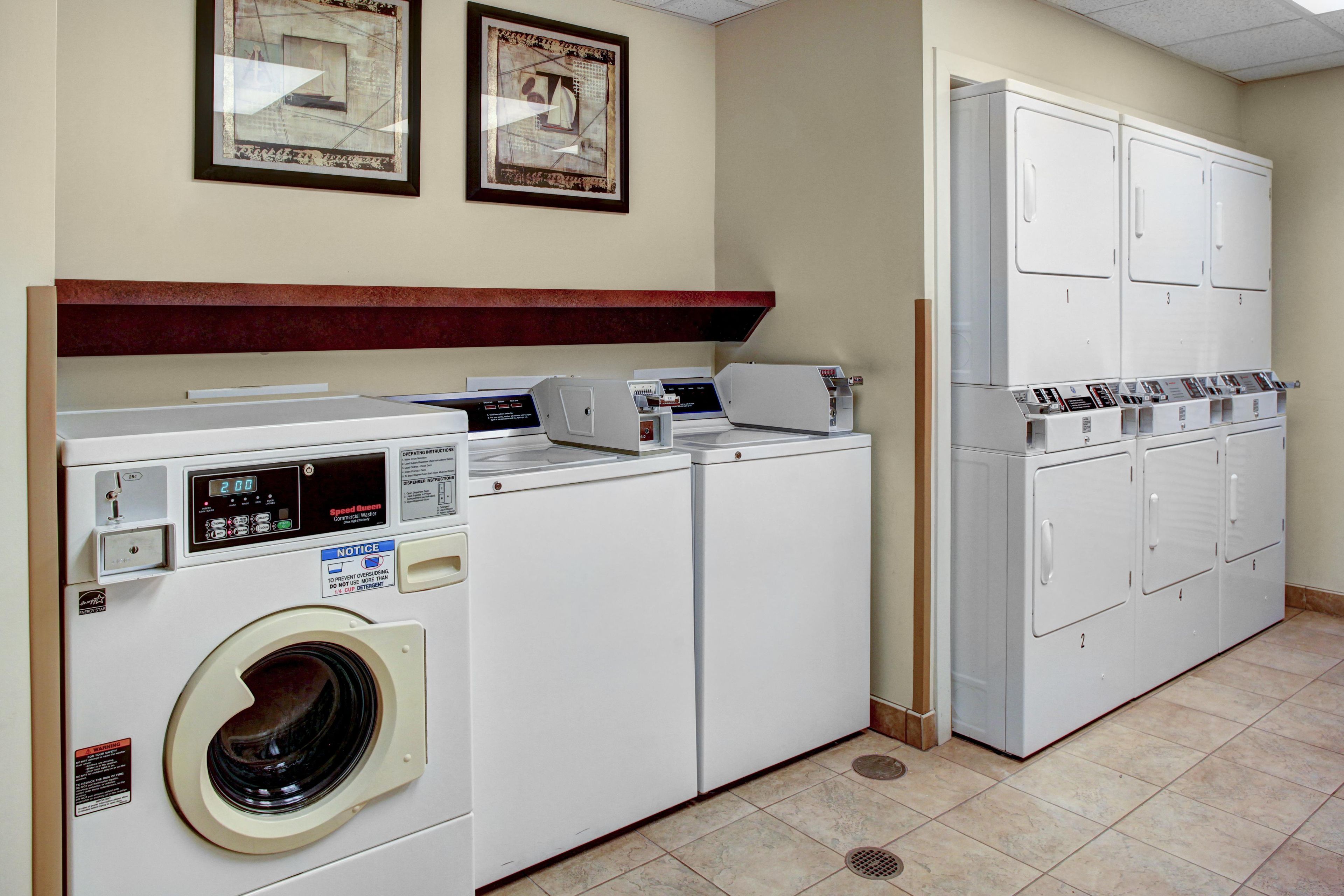 A laundry room with a front-loading washer and dryer, a control panel, and a row of cabinets.
