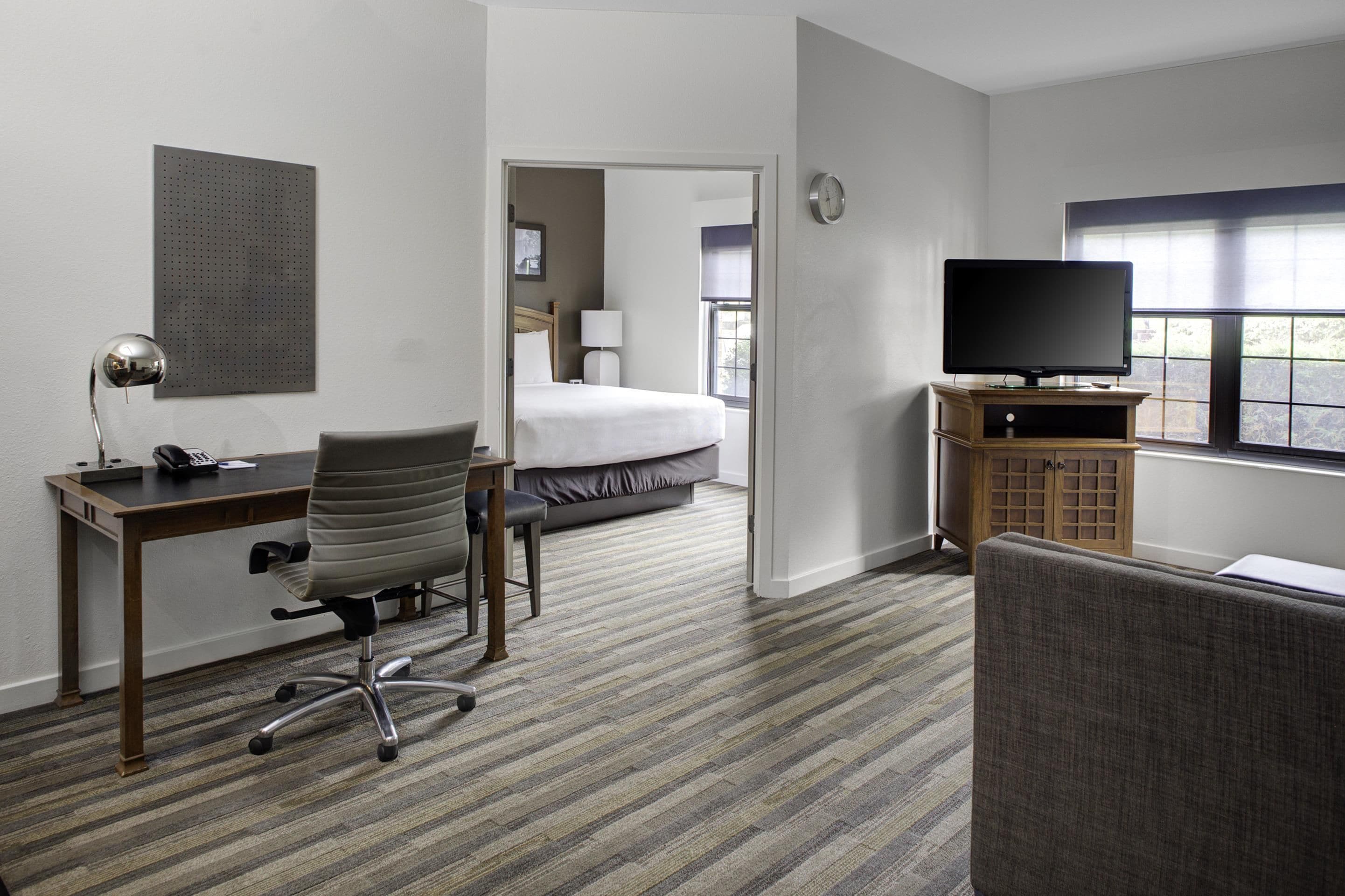 Une chambre d’hôtel avec un lit, un bureau et une chaise, une télévision et une fenêtre.
