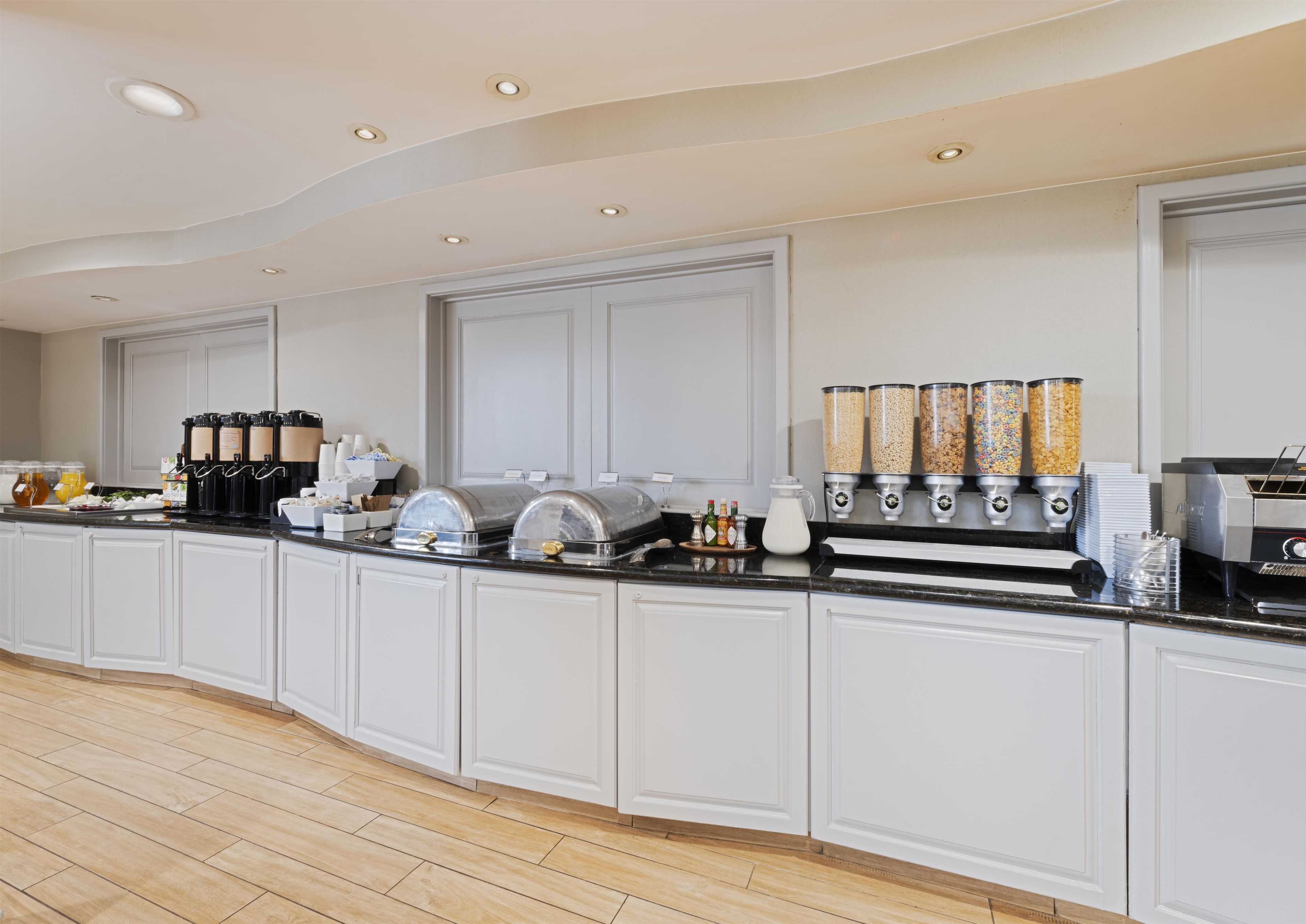 Una cocina moderna con barra de desayuno integrada, equipada con máquinas de café, dispensador de leche y una variedad de dispensadores de alimentos.