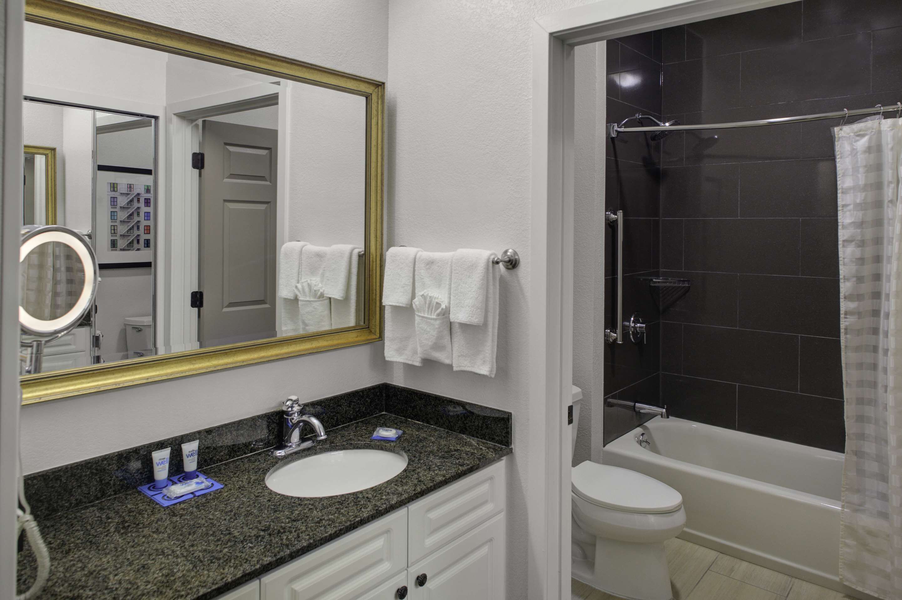 Un baño con encimera de granito, lavamanos blanco y bañera con cortina de ducha.