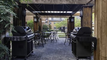 Eine Terrasse im Freien mit zwei Grillstationen, einem Tisch und Stühlen.