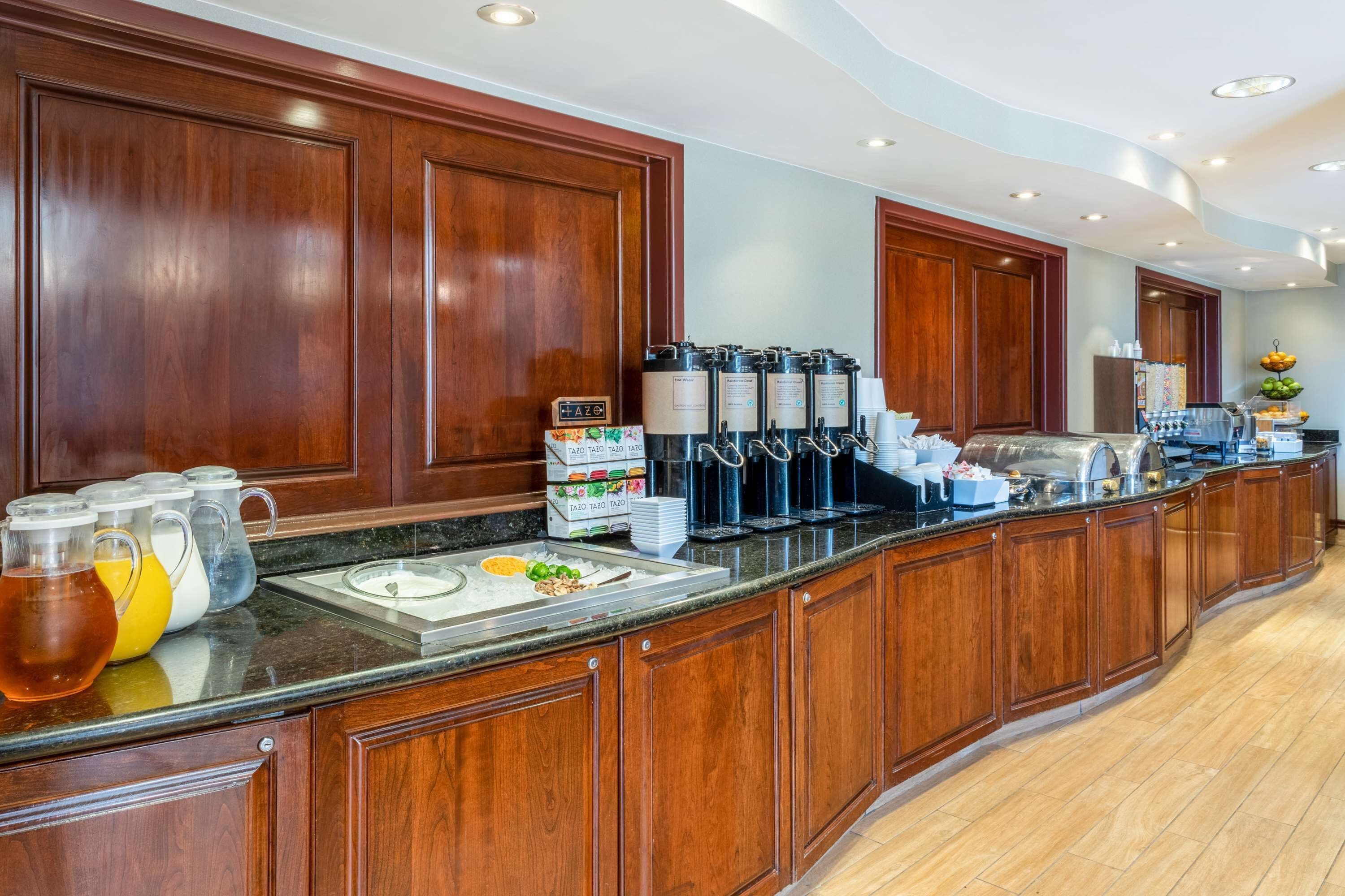 A buffet area with wooden cabinets, a marble countertop, and beverage dispensers.