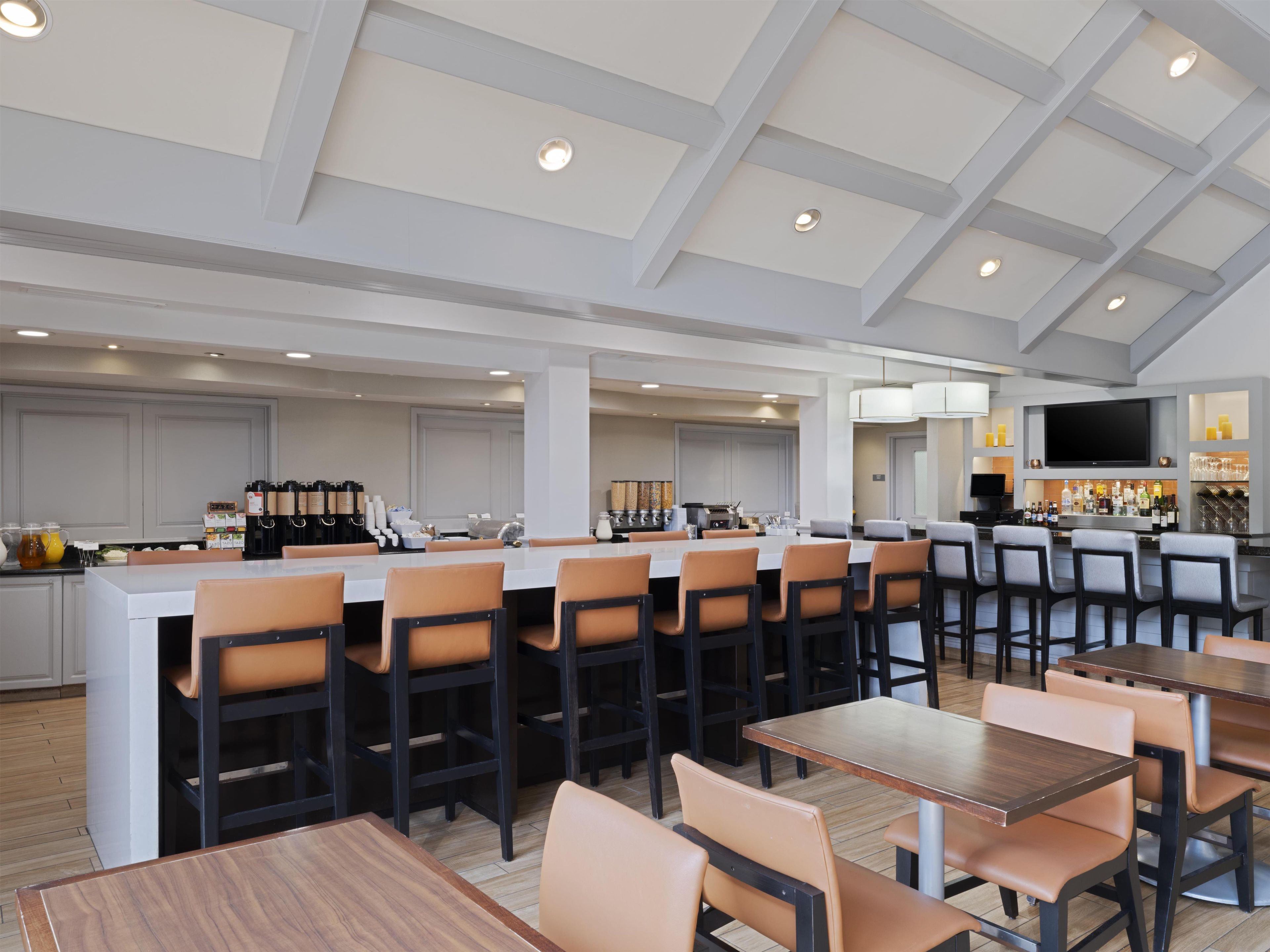 A modern dining area with high ceilings, a bar, and a kitchen in the background.