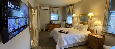 A hotel room with a bed, bedside tables, a TV mounted on the wall, a dresser, and a window with curtains.