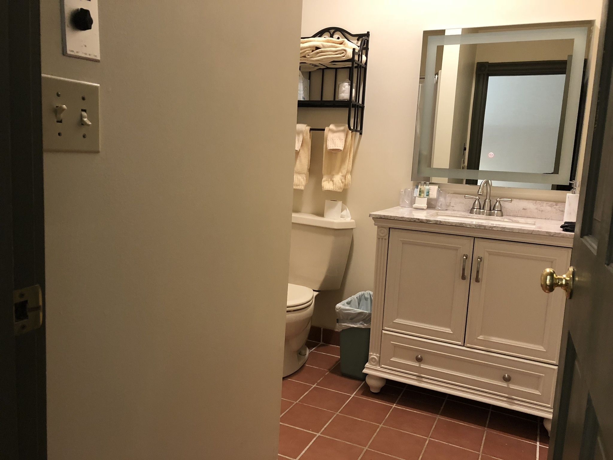 A bathroom with a toilet, sink, and a mirror above the sink. There is a trash bin next to the toilet.