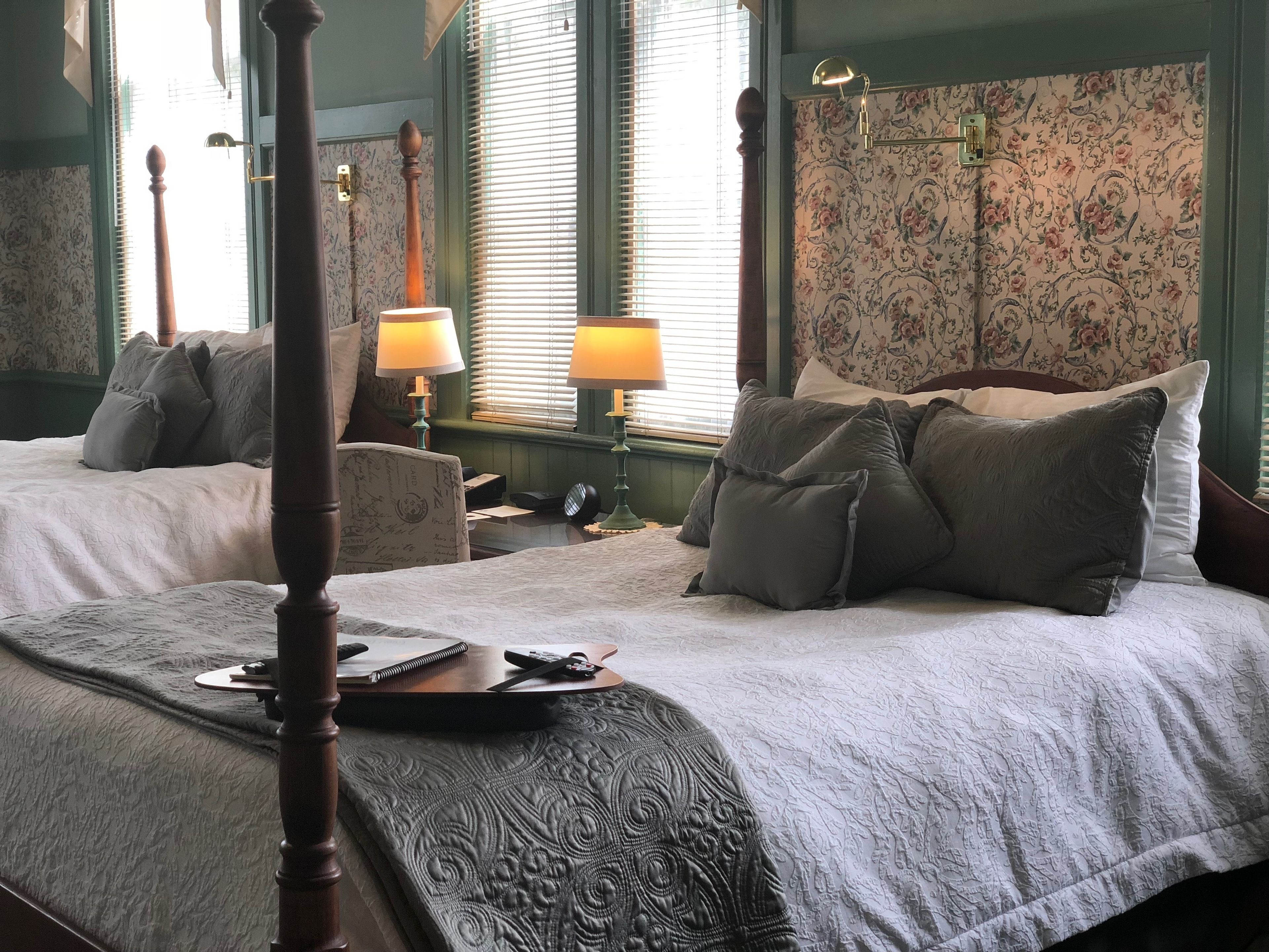 A bedroom with two beds, a wooden four-poster bed, a chair, a bedside table, and a lamp.
