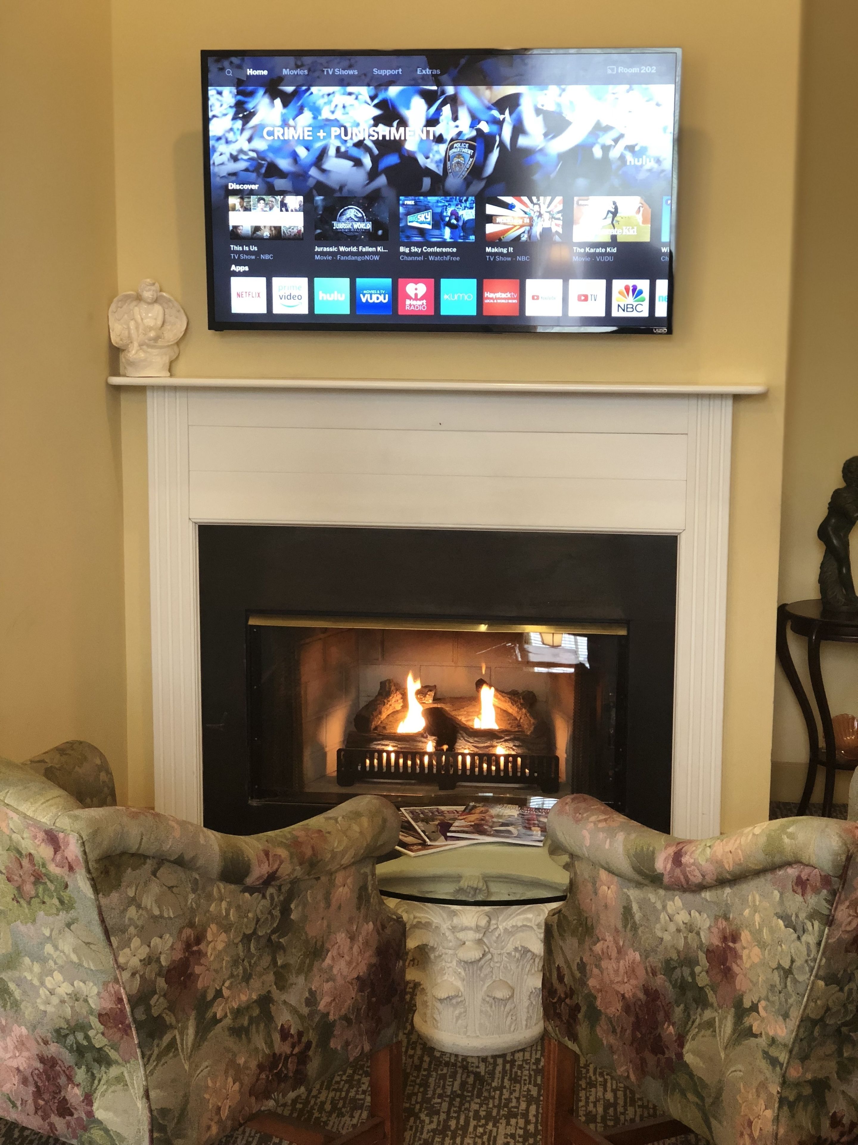 Un salón con chimenea, un televisor de pantalla plana montado sobre ella y muebles con estampado floral.