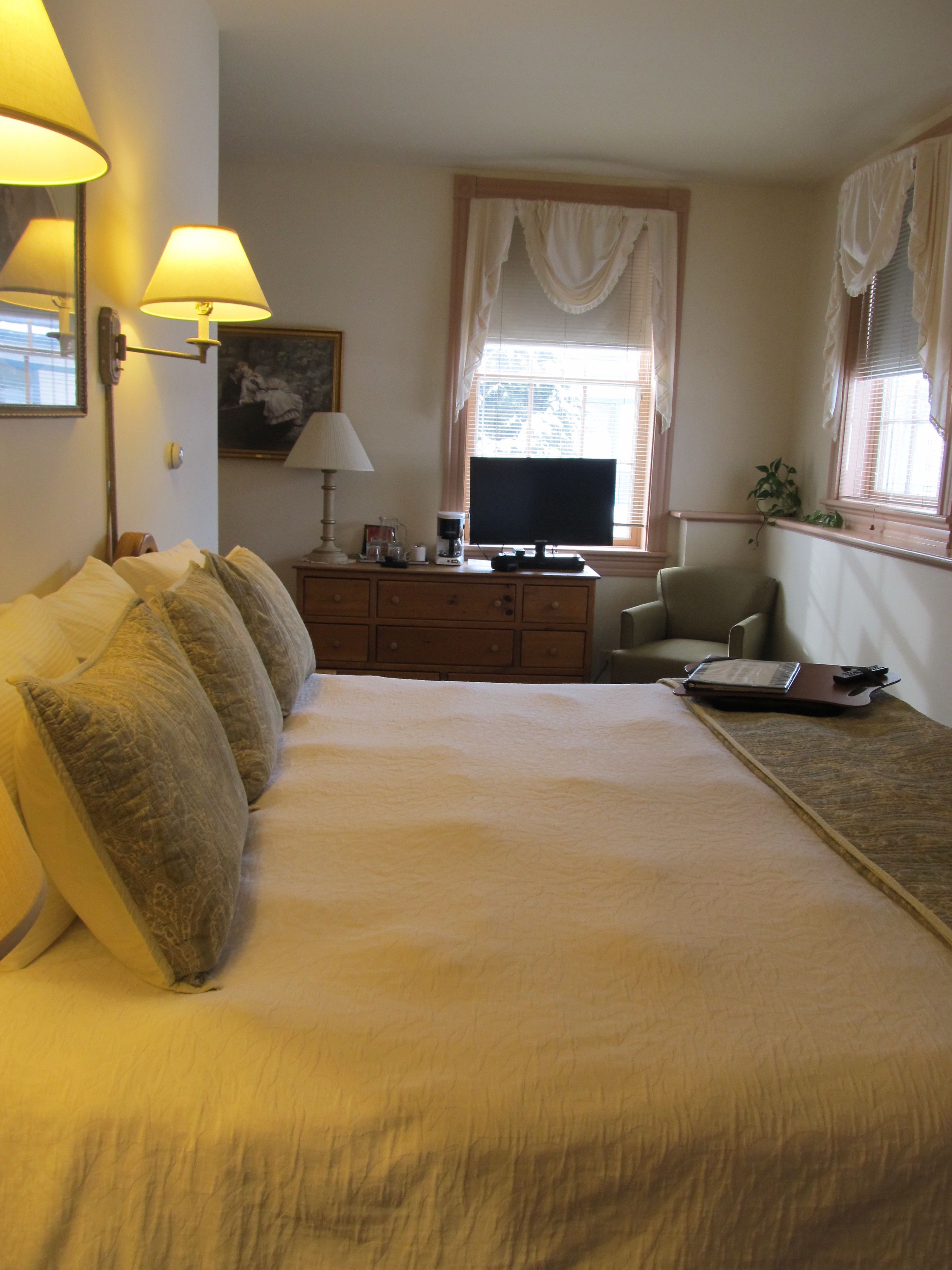 A bedroom with a large bed, a desk, a chair, a television, and a window with curtains.