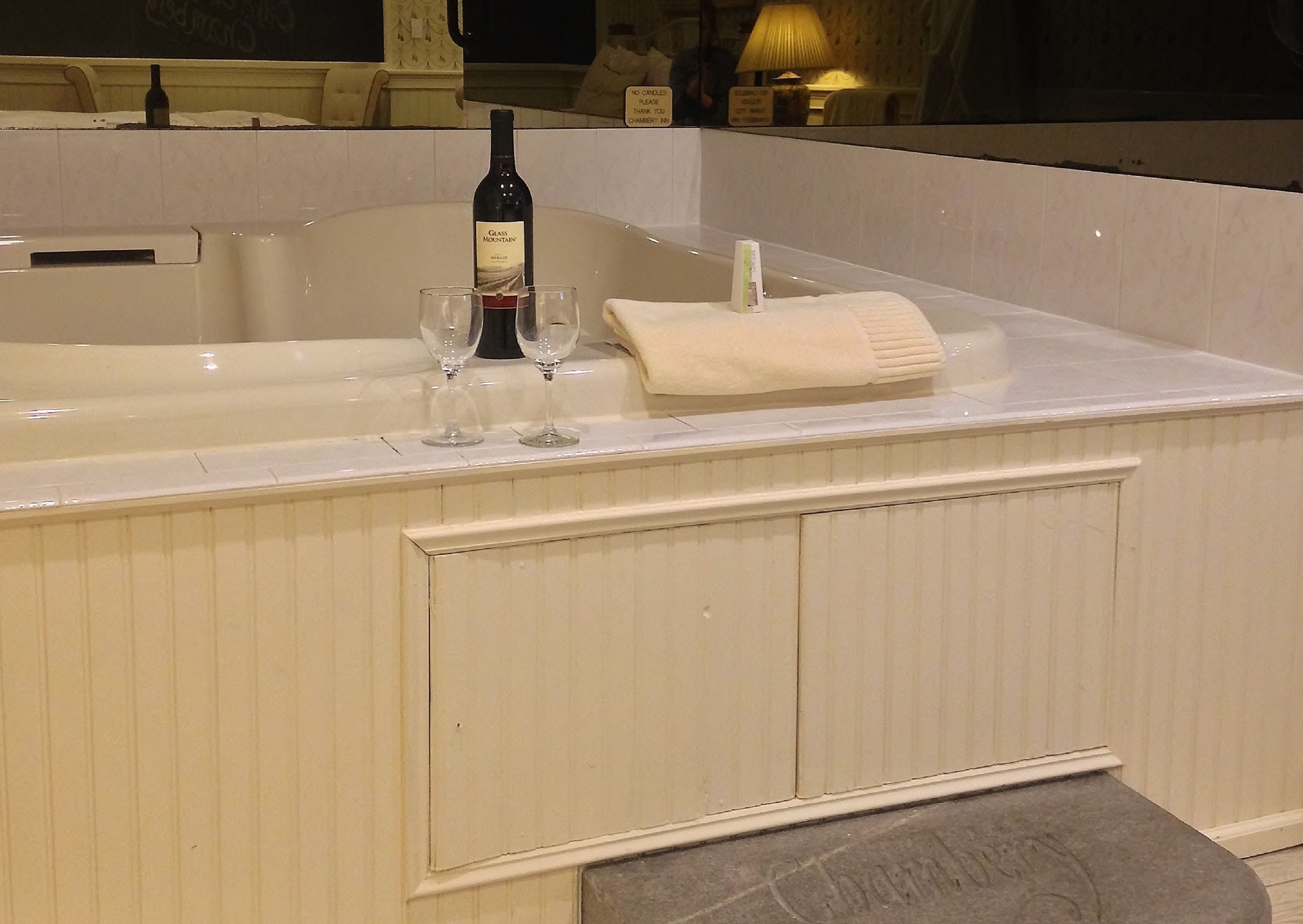 A bathtub with a bottle of wine and two glasses.