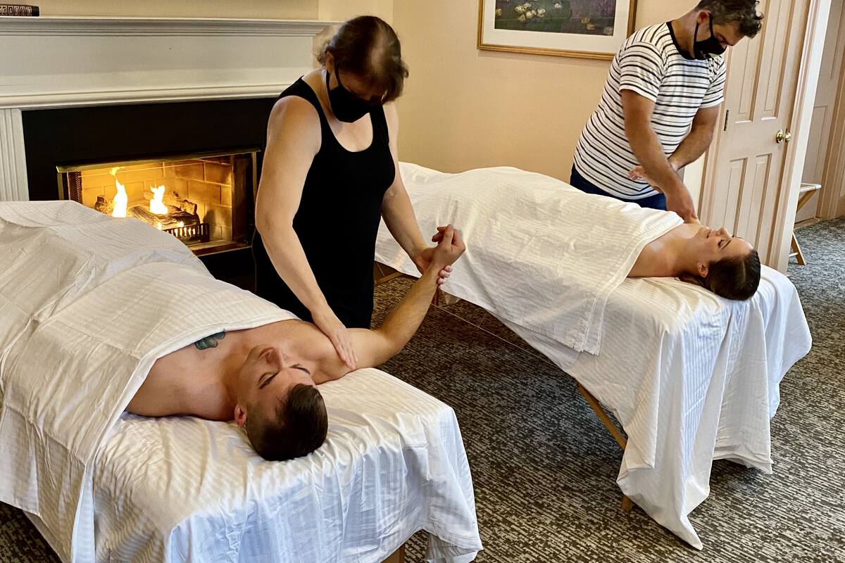 A massage therapy room with two massage tables, a fireplace, and a painting on the wall.