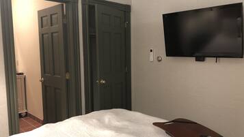 Una habitación de hotel con una cama, un control remoto, un televisor montado en la pared y dos puertas.