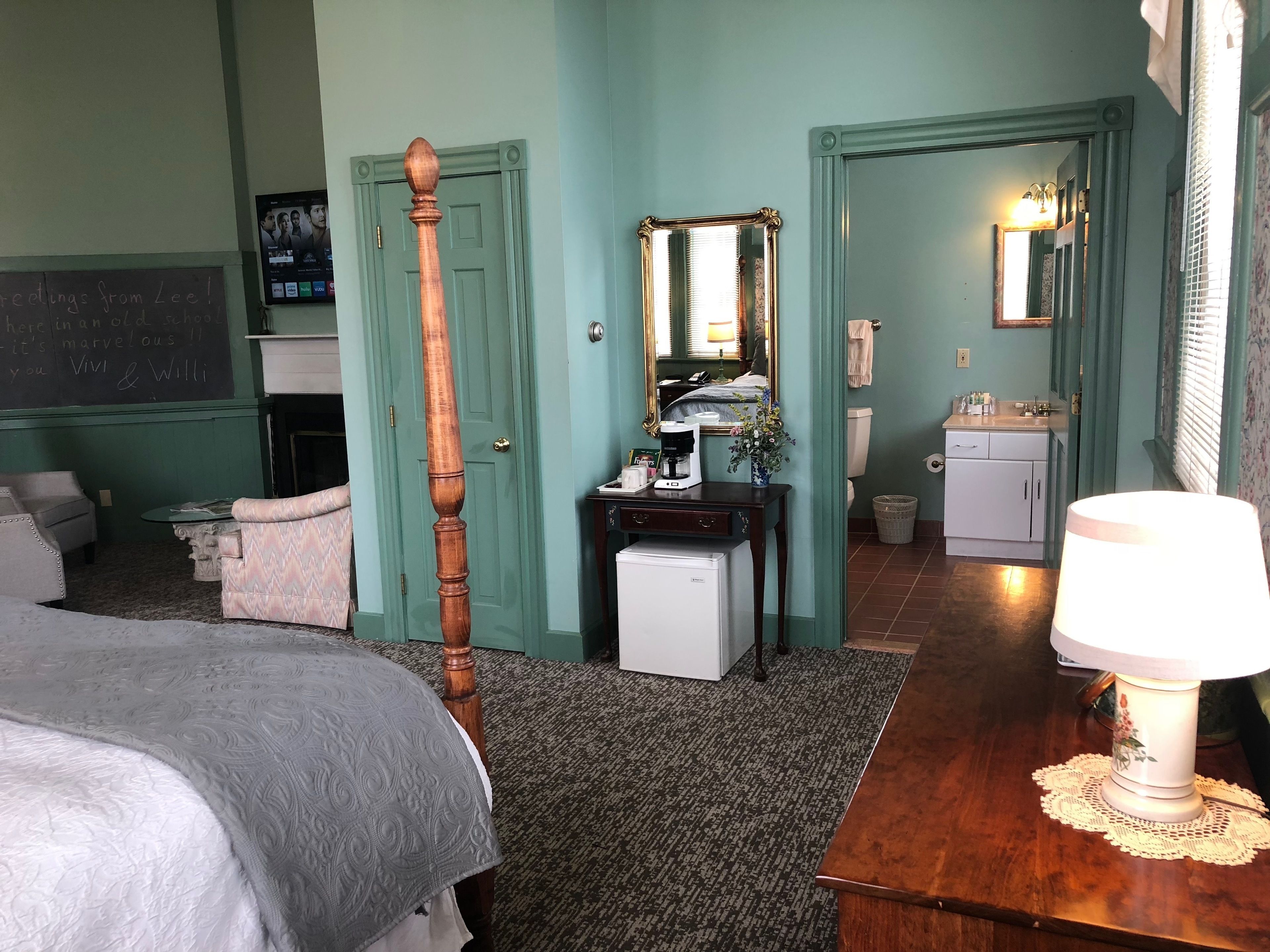 A bedroom with a bed, a dresser, a mirror, a coffee maker, and a lamp.