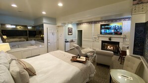 A hotel room with a large bed, a TV mounted above a fireplace, a desk, and a seating area with chairs. - Chambery Inn (Lee)